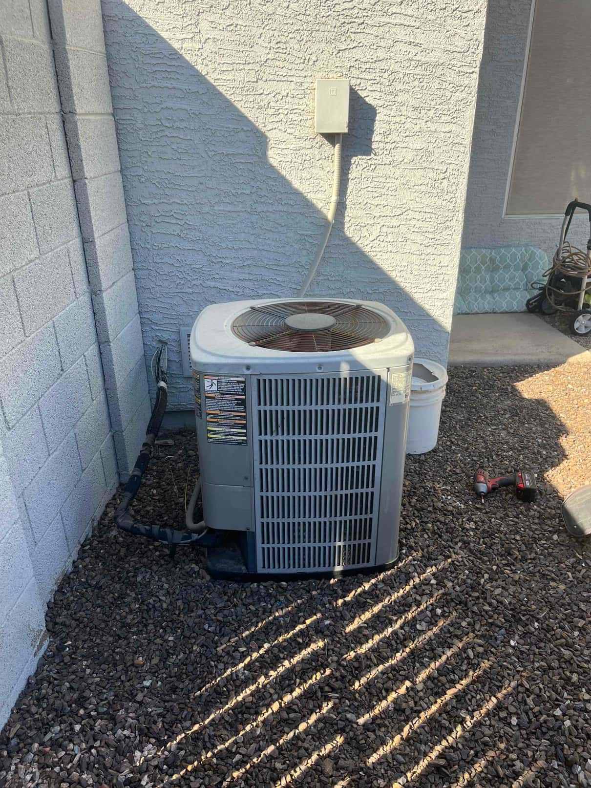 Outdoor condenser unit beside house with insulated refrigerant lines and wall-mounted disconnect visible.