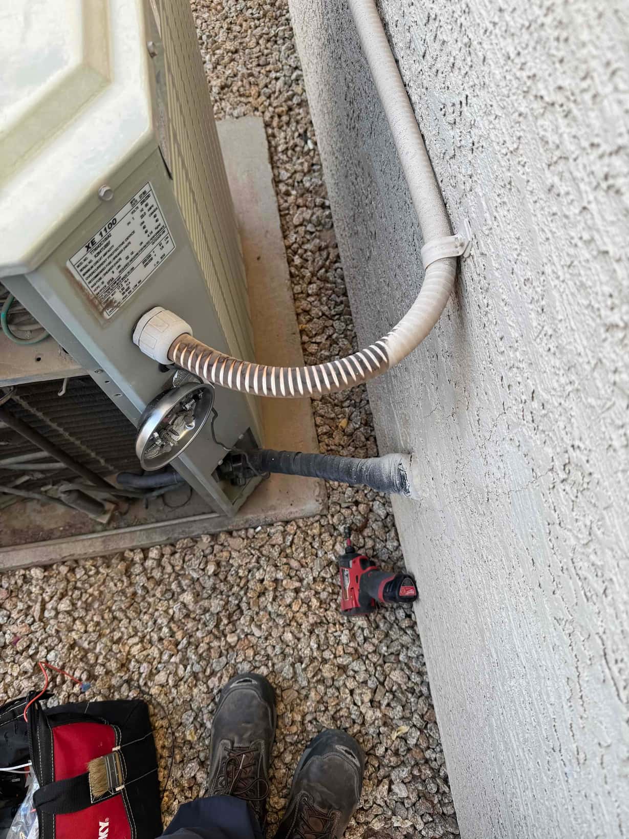 Outdoor condenser unit with service disconnect, flexible electrical conduit, and insulated refrigerant line entering the stucco wall.