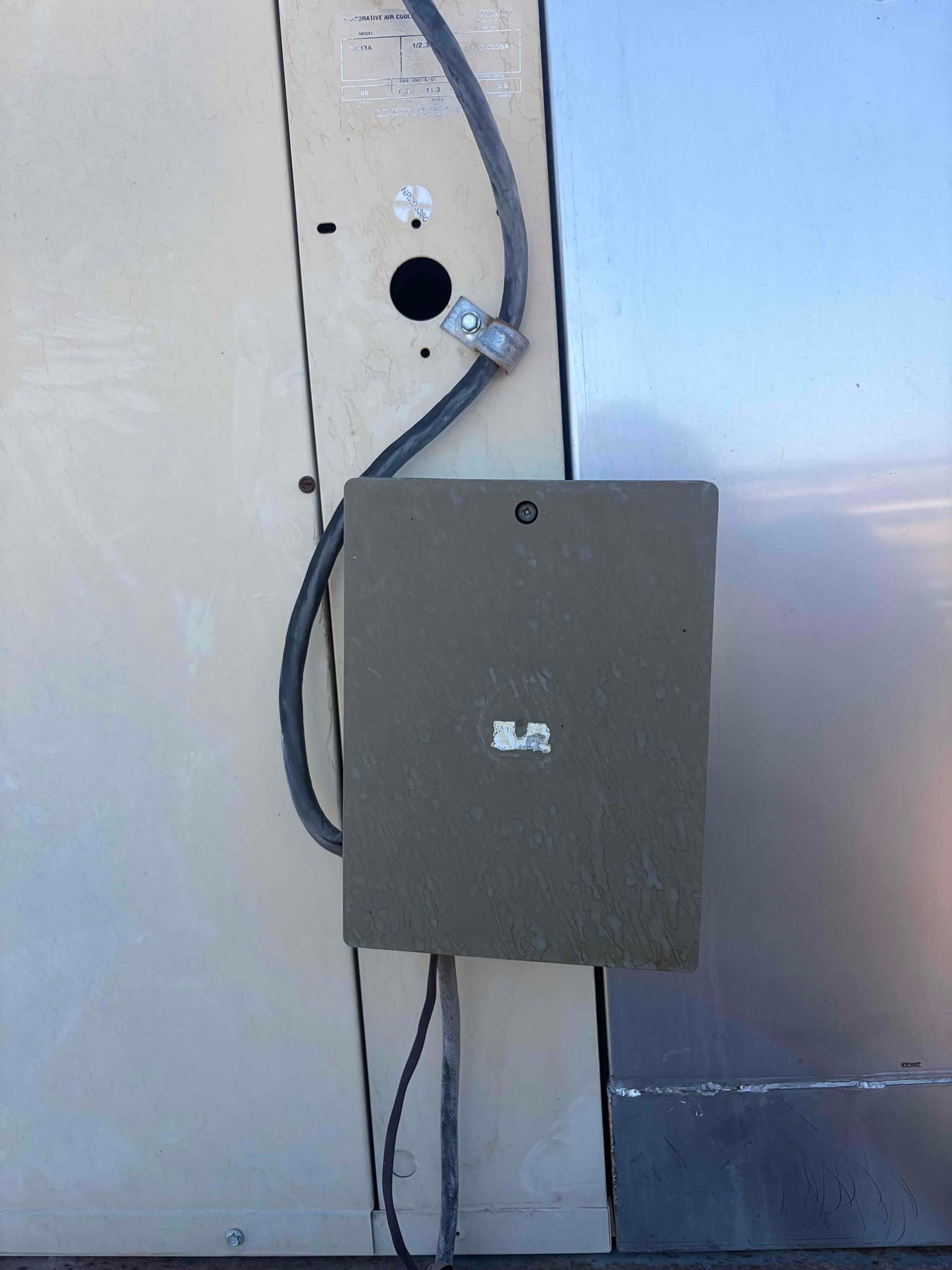 Outdoor electrical disconnect box with flexible conduit and open knockout on HVAC cabinet.