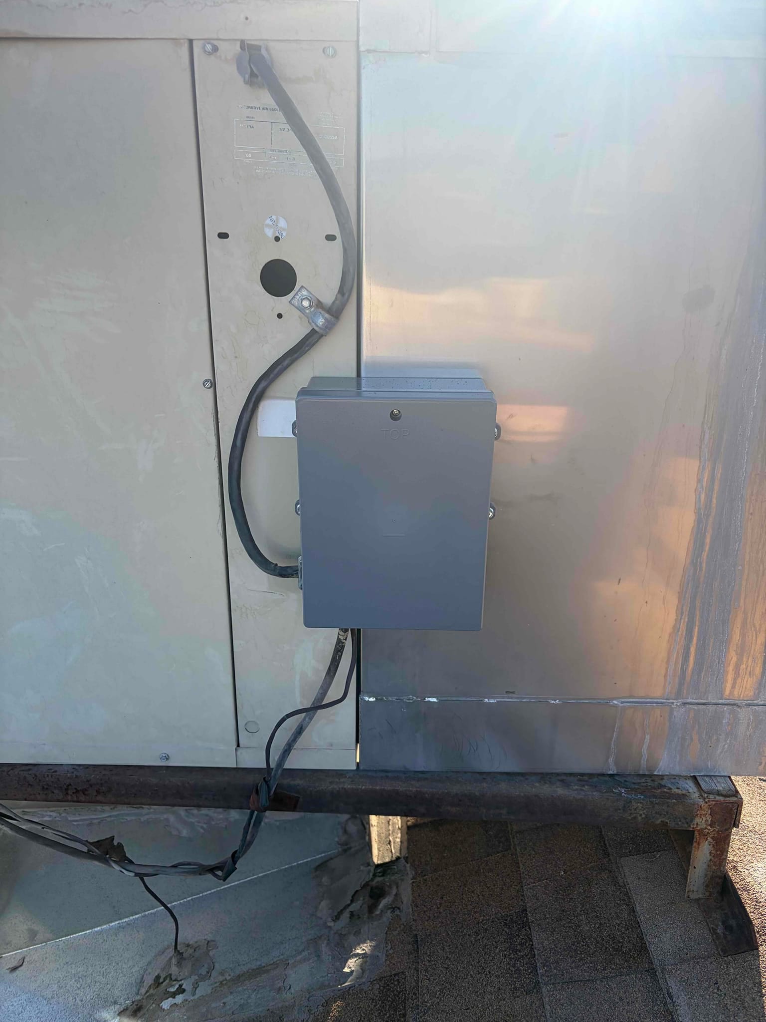Outdoor HVAC unit side panel with weatherproof electrical disconnect box and flexible conduit installed on support.
