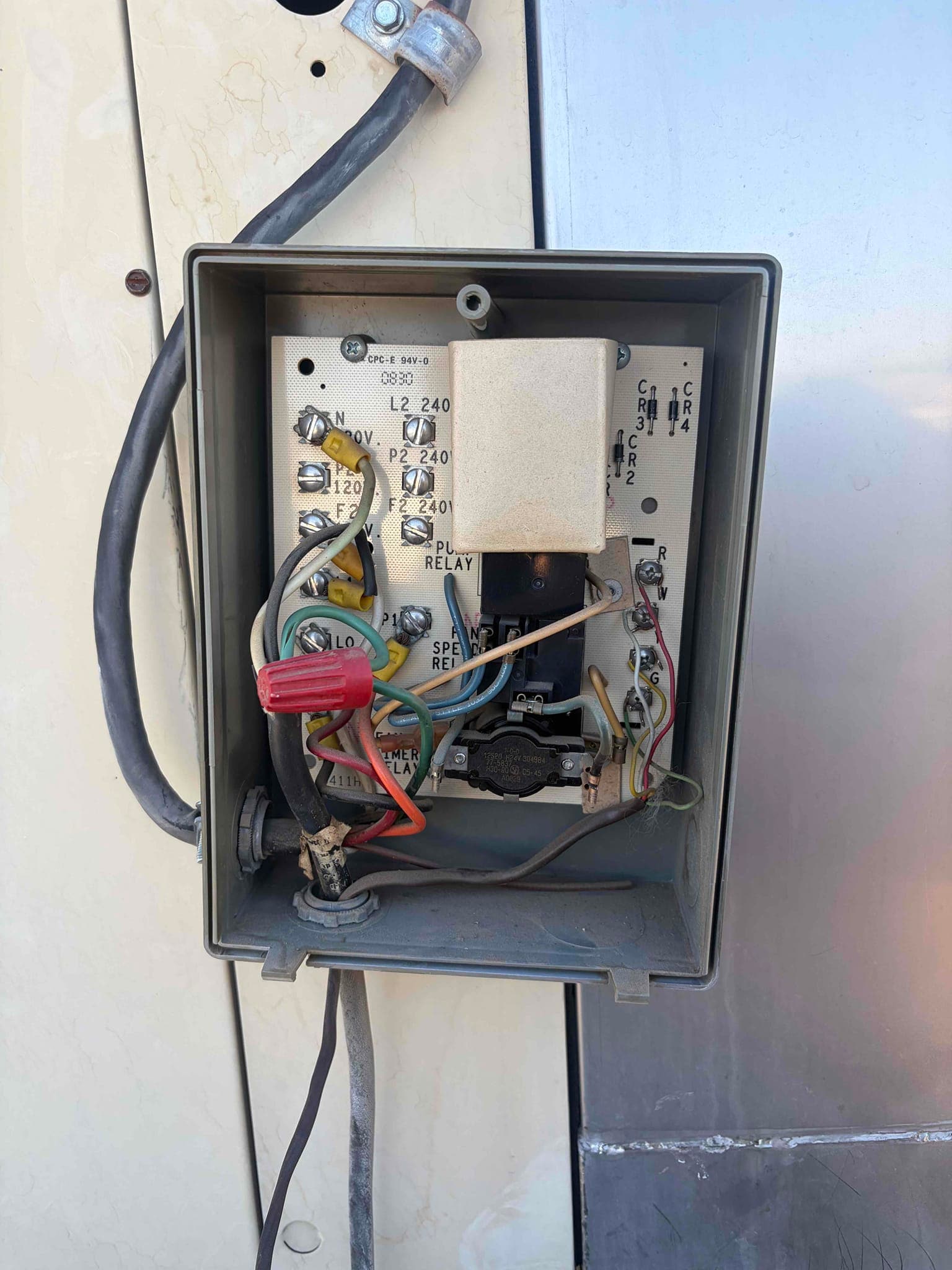 Outdoor unit control box open, showing relays, wiring, terminal labels, and a timer with connected wires.
