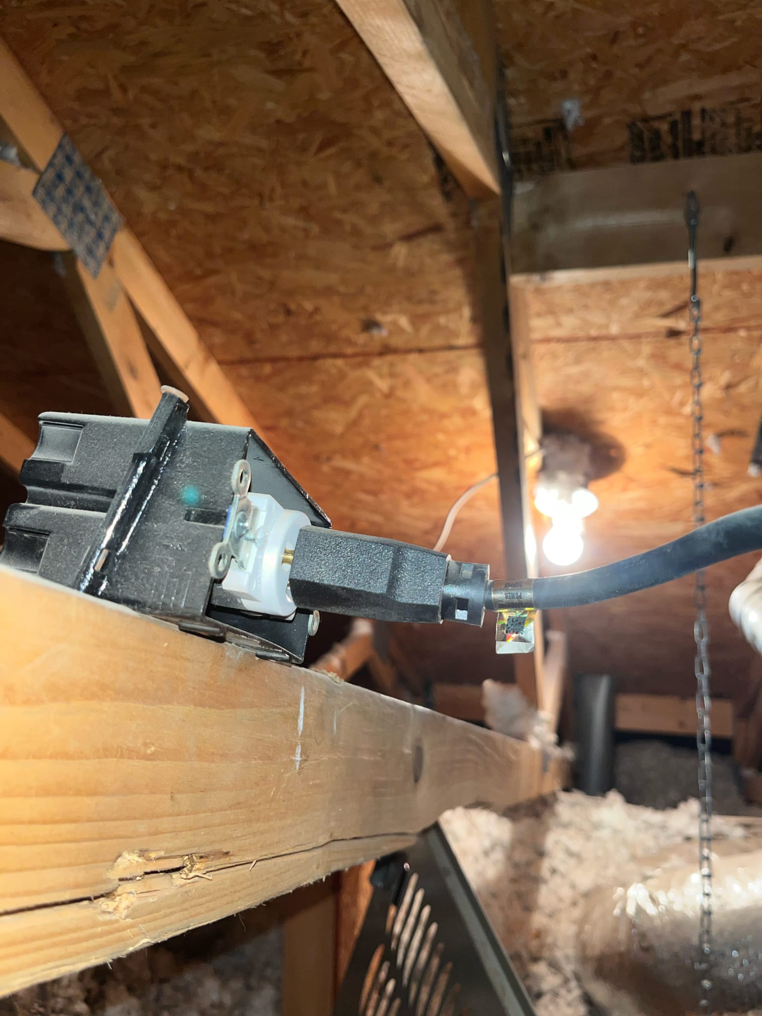 Outlet box with a power cord plugged in, mounted on a joist beside attic ductwork and insulation.