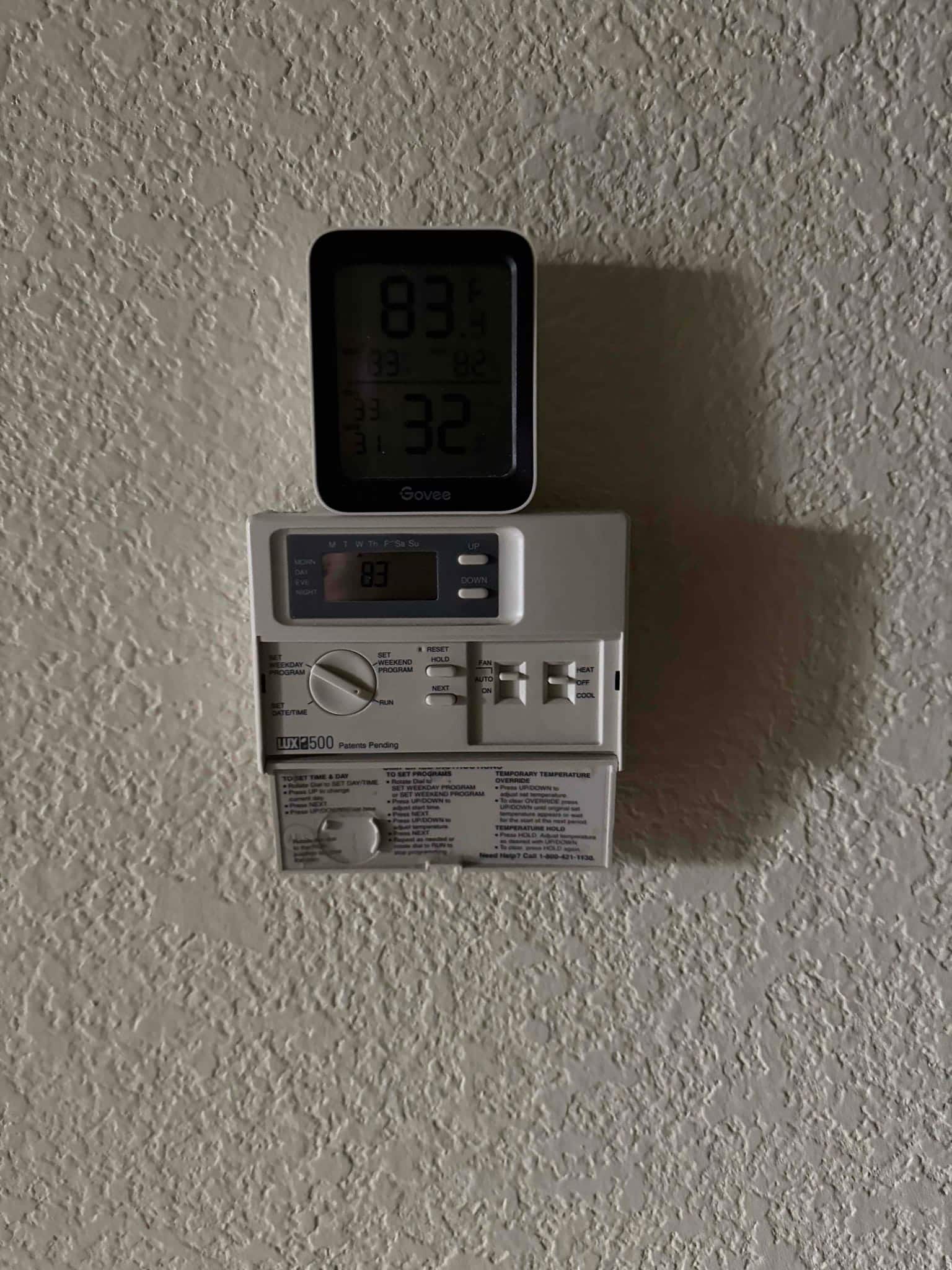 Programmable wall thermostat with sliding fan and mode switches, with a compact digital temperature and humidity display sitting on top.