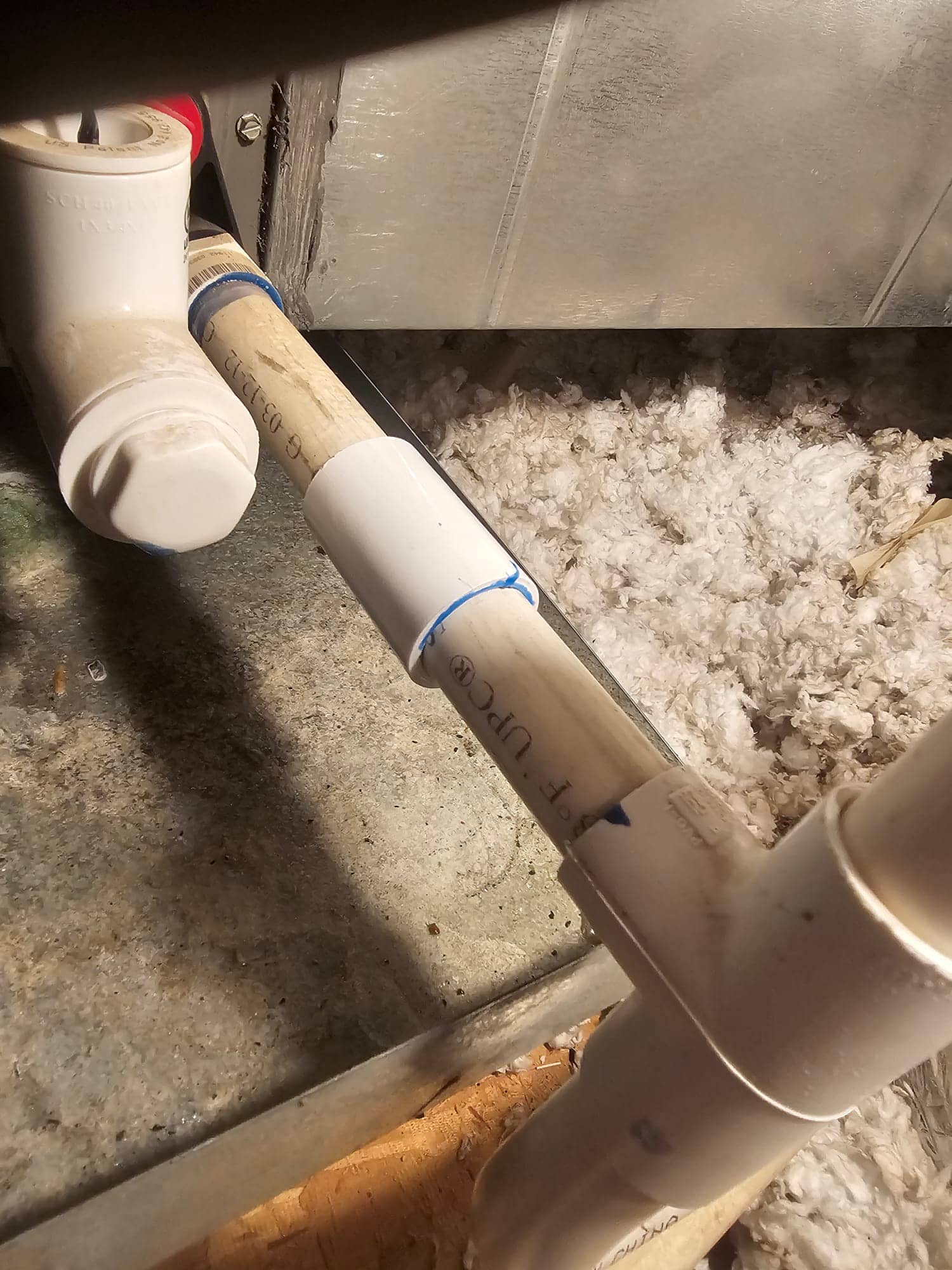 PVC condensate drain piping with cleanout tee and capped vent near an air handler, blue primer joints.