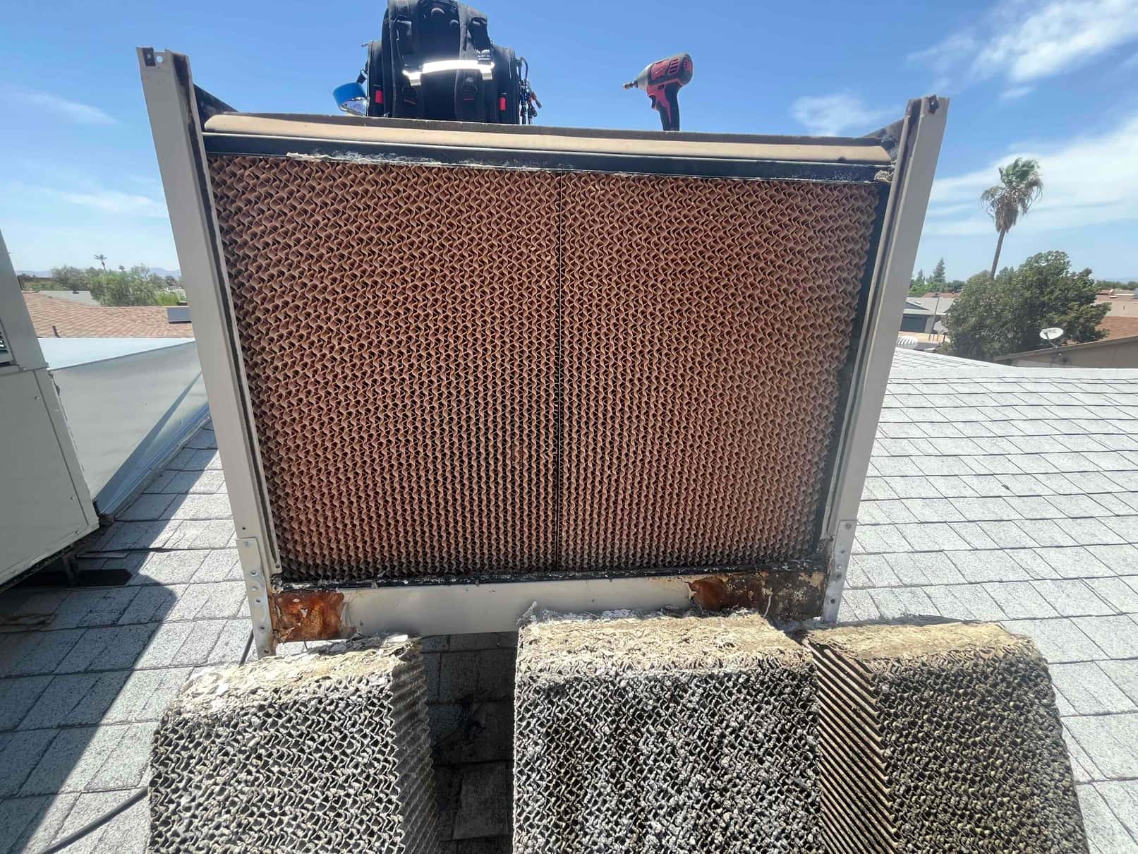 Rooftop evaporative cooler with two media pads removed, center pad installed, and visible rust along the lower frame.