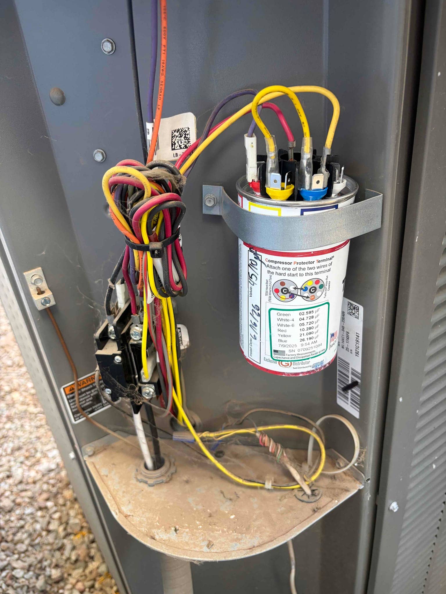 Run capacitor with color-coded terminals and printed microfarad values, wired inside the outdoor condenser cabinet near the contactor.