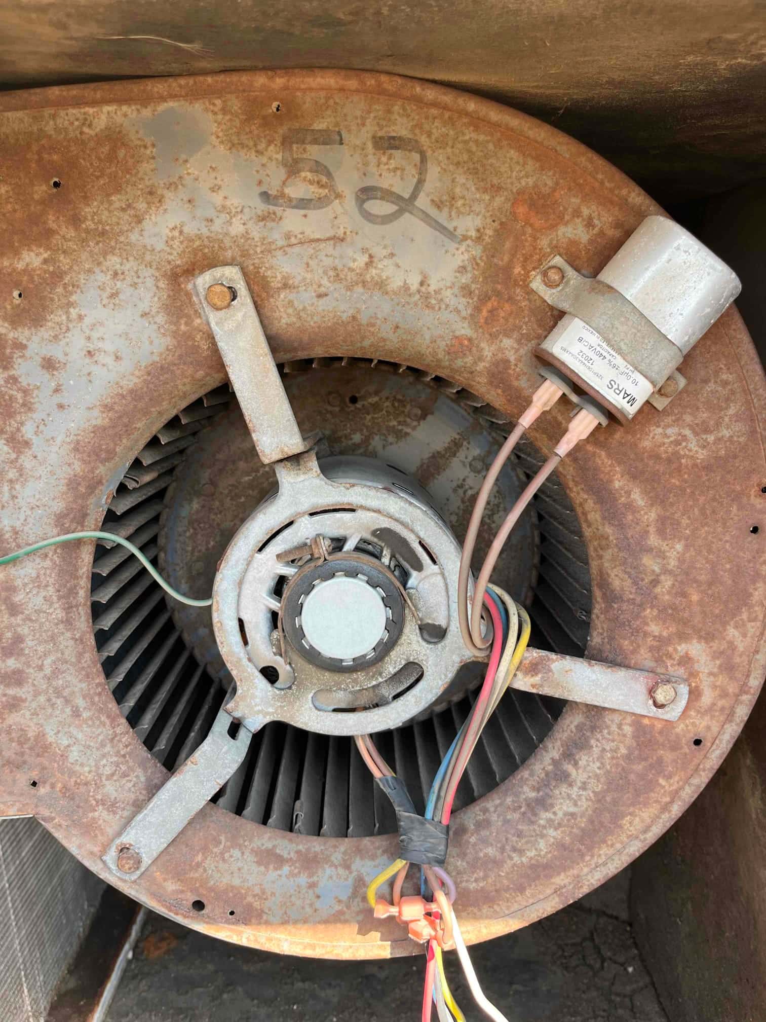 Rusted blower housing and wheel with an external run capacitor and connected wiring visible.