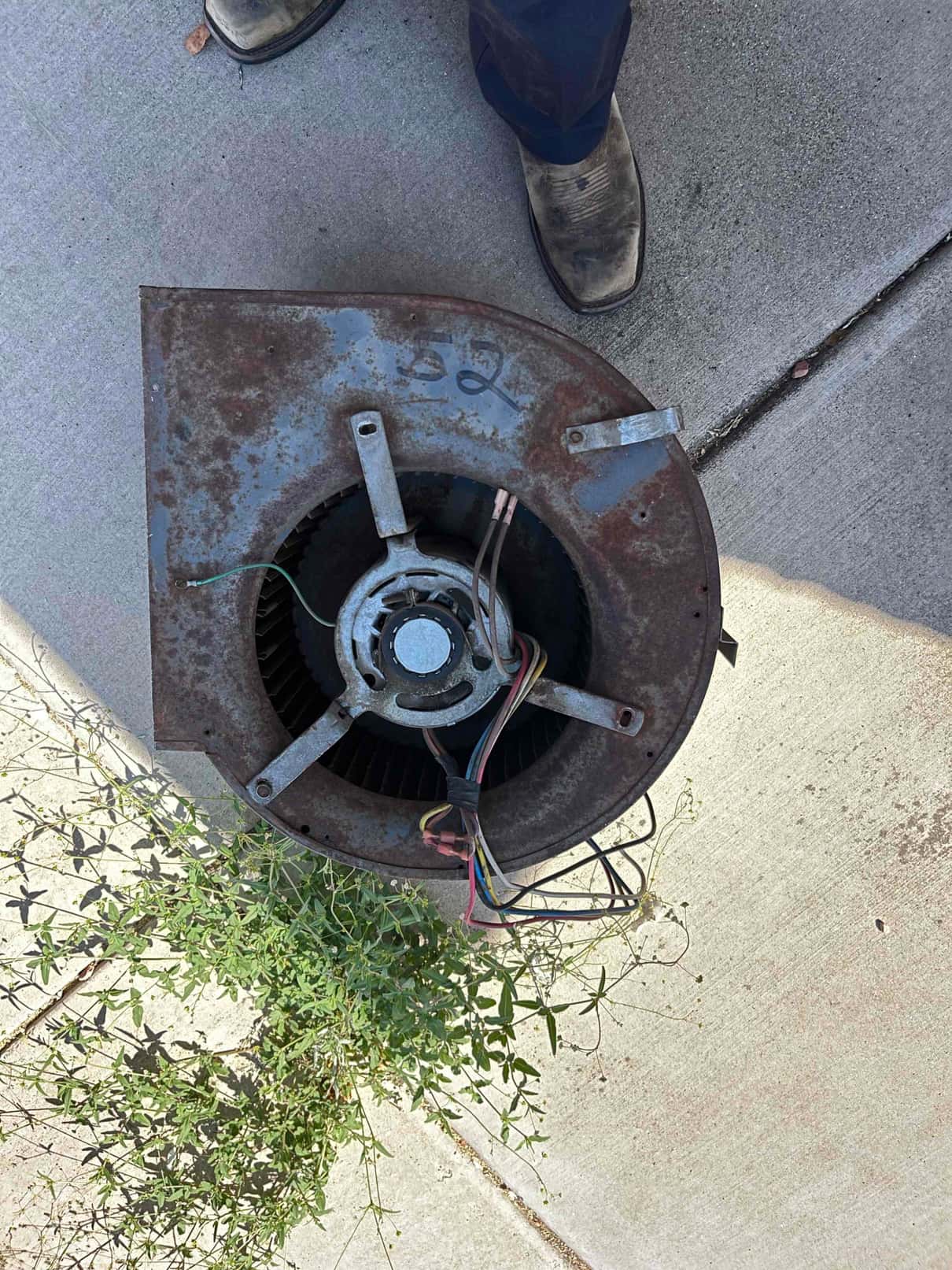Rusty blower housing and motor assembly with squirrel-cage wheel and wiring visible on the ground.