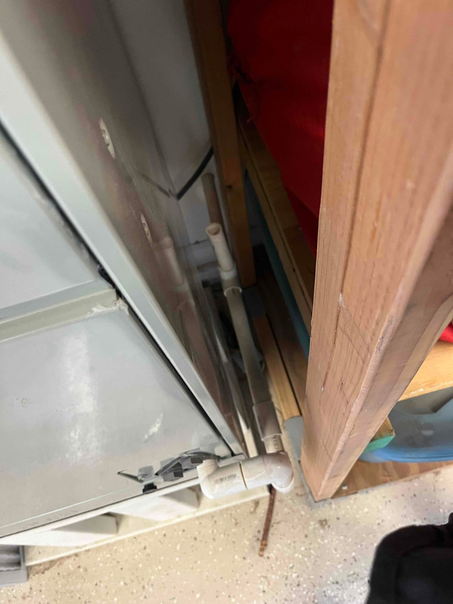 Side of indoor air handler beside framing, showing PVC condensate drain with tee, elbow, and cleanout.