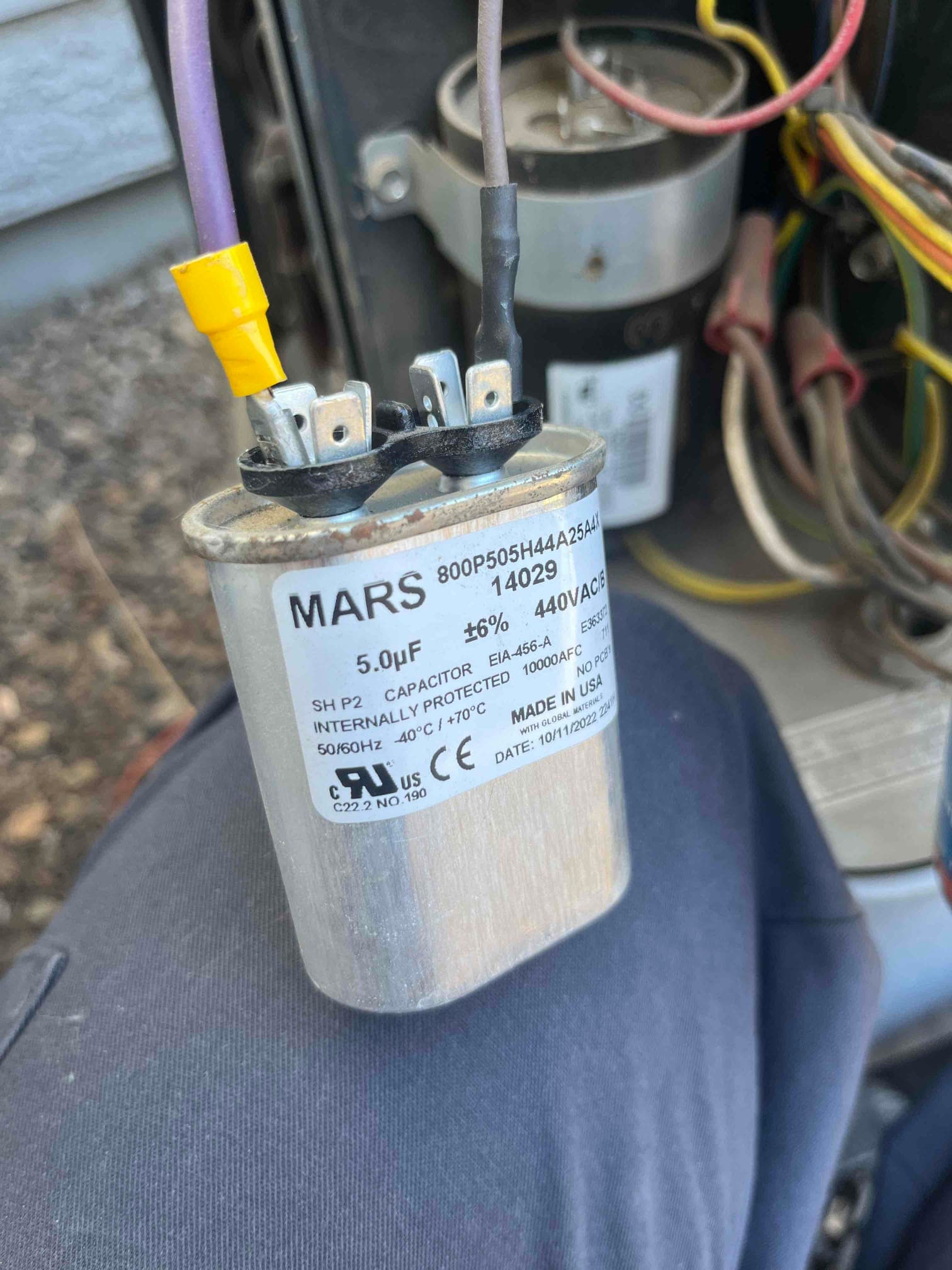 Single run capacitor labeled 5.0 μF 440VAC with two wires connected to spade terminals inside the condenser unit.
