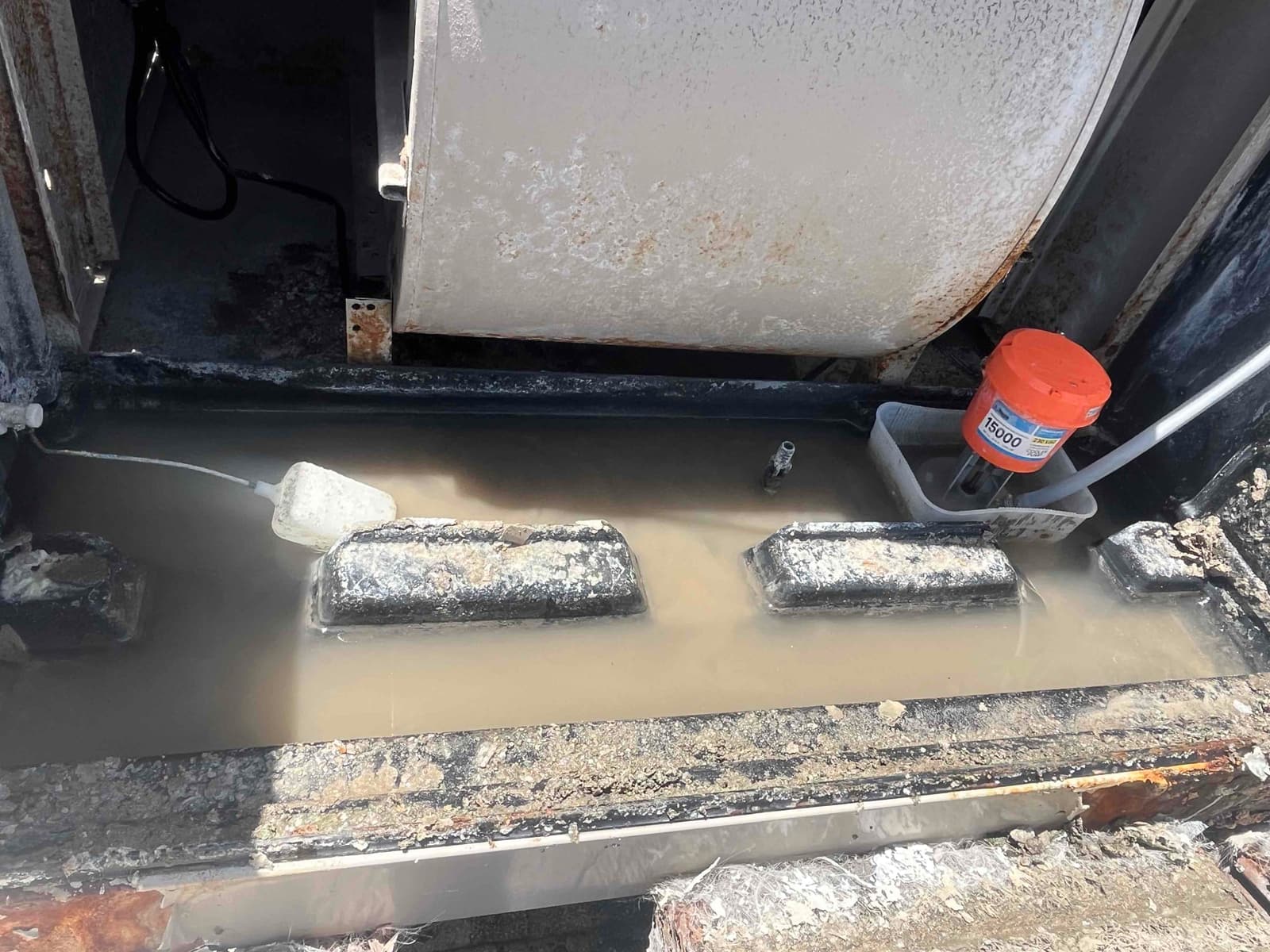 Standing murky water in an HVAC drain pan with a float device, tubing, and visible rust.