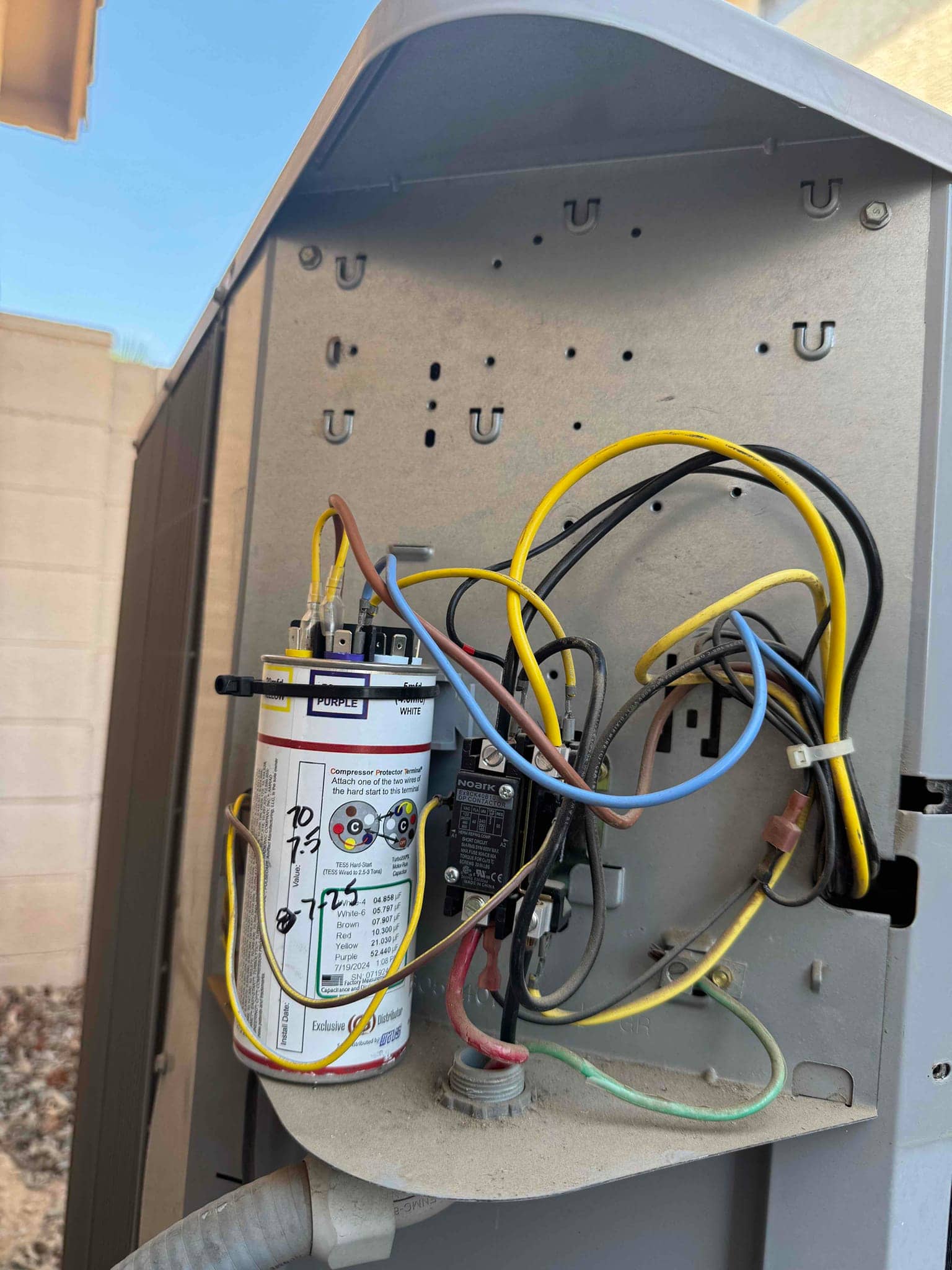 Start assist capacitor with wiring connected, alongside contactor and conductors inside an outdoor condenser control compartment.