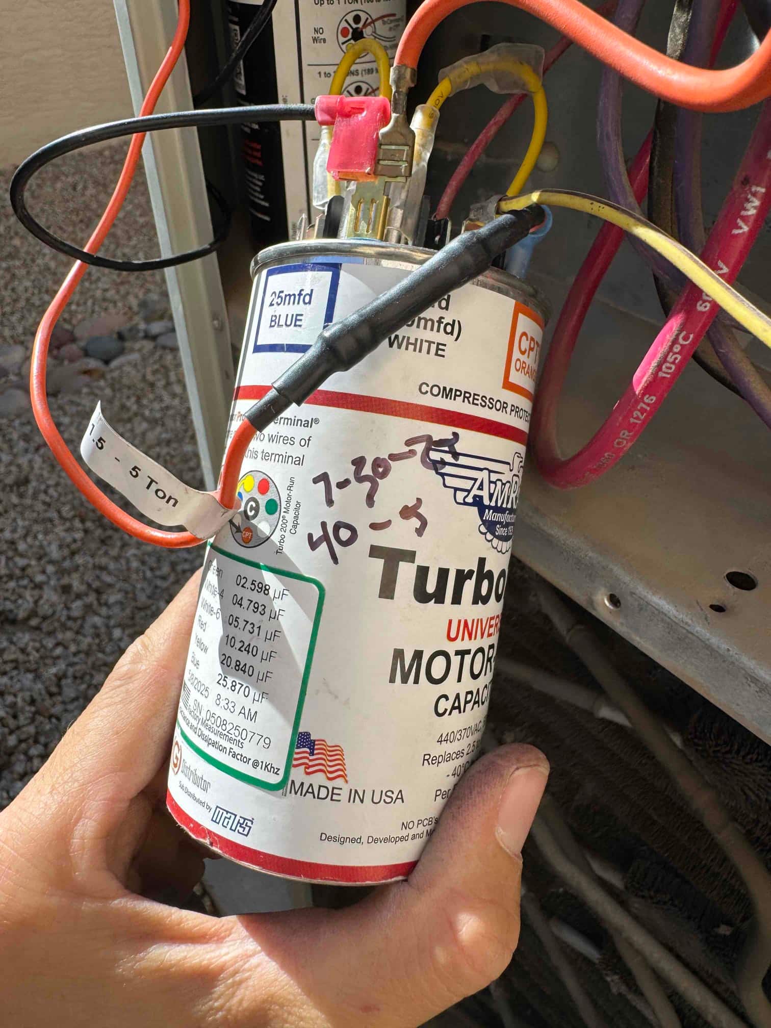 Universal motor run capacitor labeled 25 mfd BLUE, shown with connected wires and spade terminals inside the condenser cabinet.
