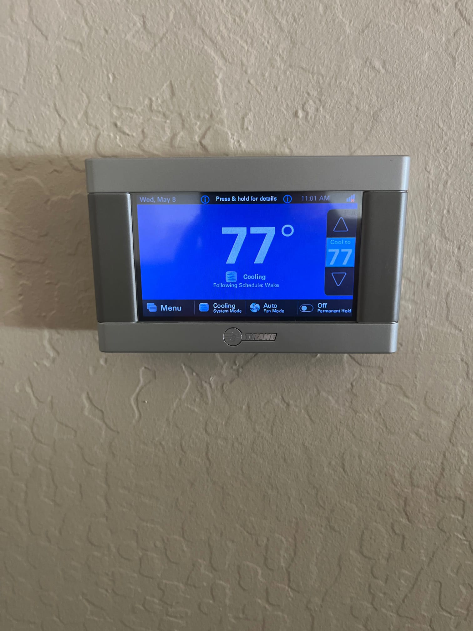Wall-mounted digital thermostat display shows 77 degrees, set to cool to 77, with cooling mode active.