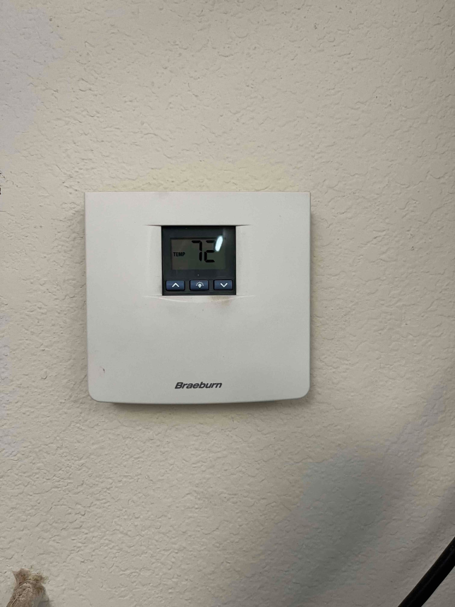 Wall-mounted digital thermostat displays 72 with temperature label and arrow buttons beneath the screen.
