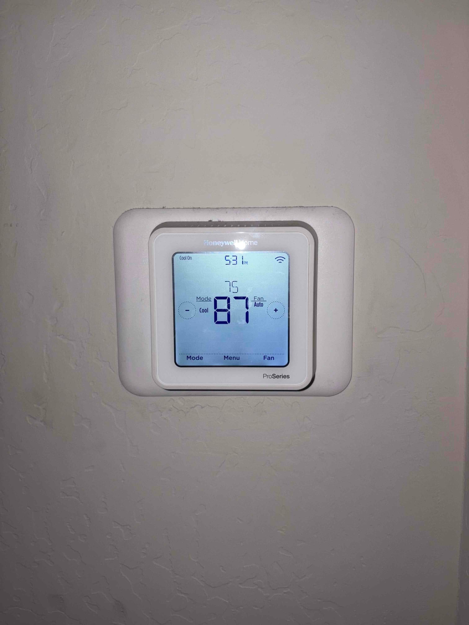 Wall-mounted digital thermostat displays 87 room temperature with cooling mode on and setpoint at 75.