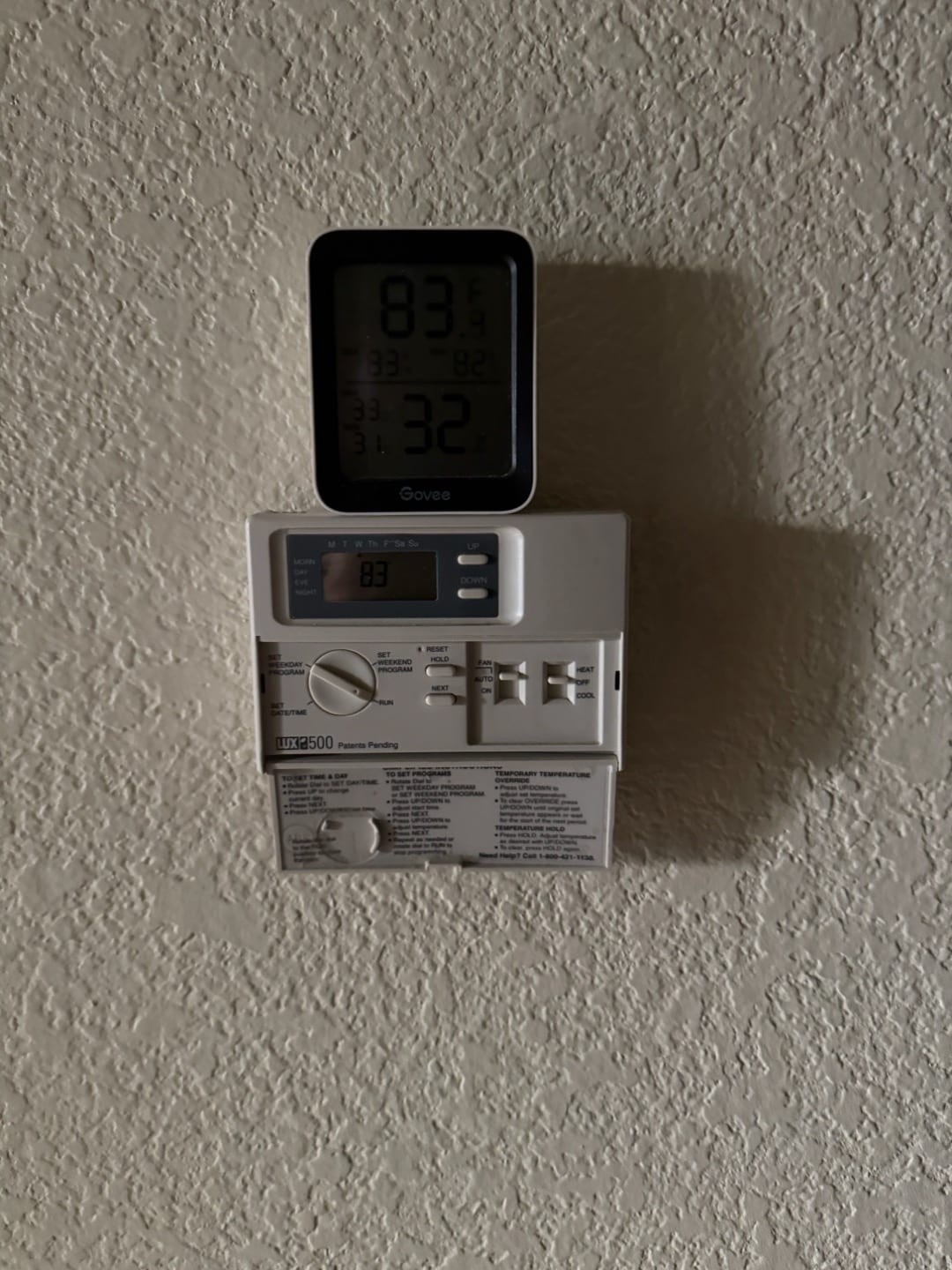Wall-mounted programmable thermostat with cover open, with a separate digital temperature and humidity display positioned on top.
