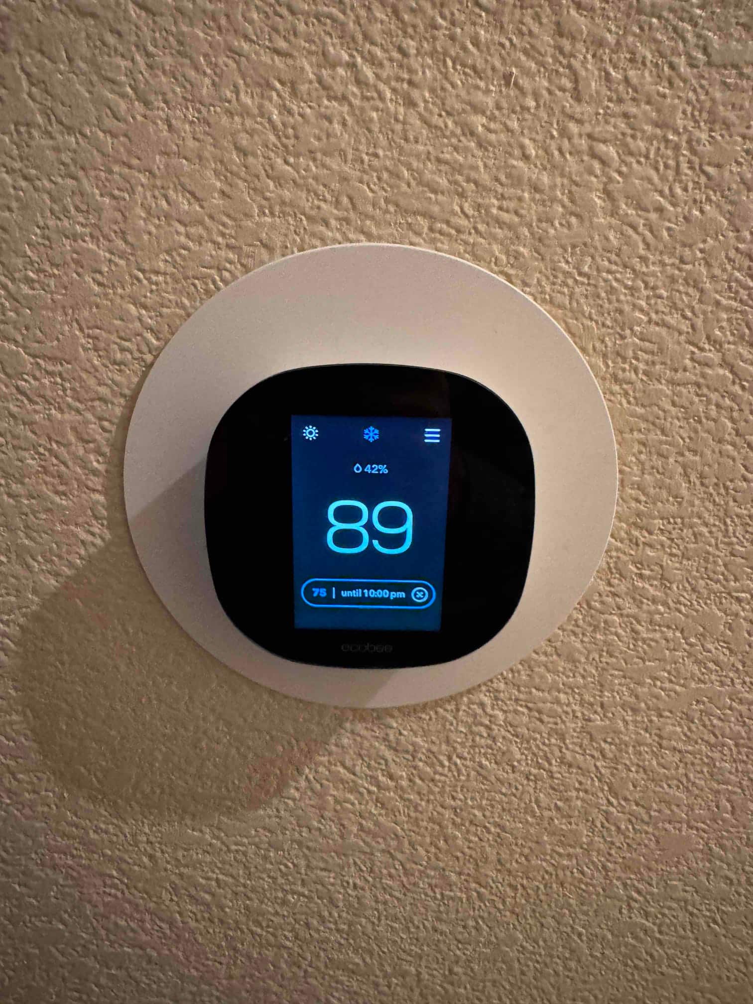 Wall-mounted smart thermostat display shows indoor temperature 89 and humidity 42%, with a cooling setpoint of 75 until 10:00 pm.