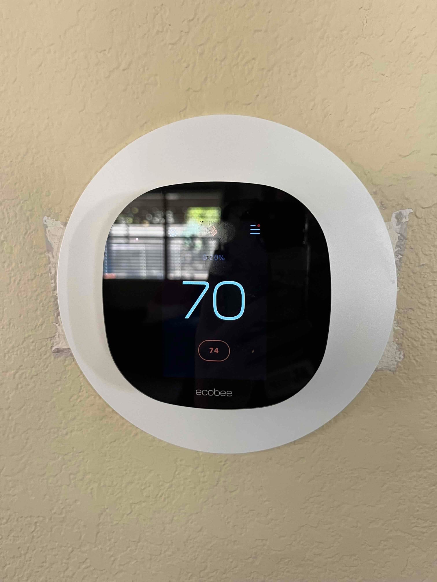 Wall-mounted thermostat displays a 70° setpoint with 74° indoor temperature, installed on a textured wall.