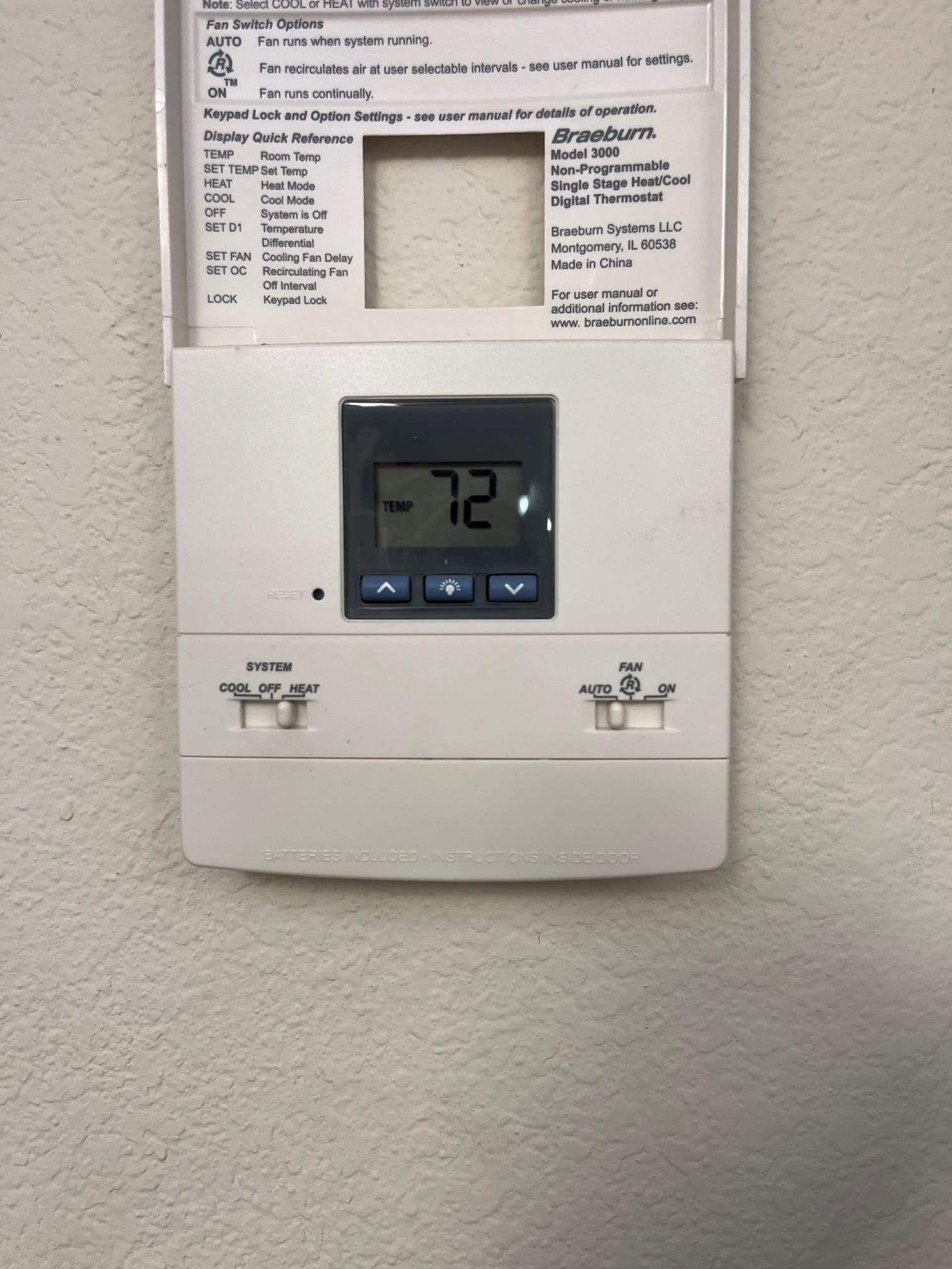 Wall-mounted thermostat with open cover and digital display reading 72, with system and fan slider switches visible.