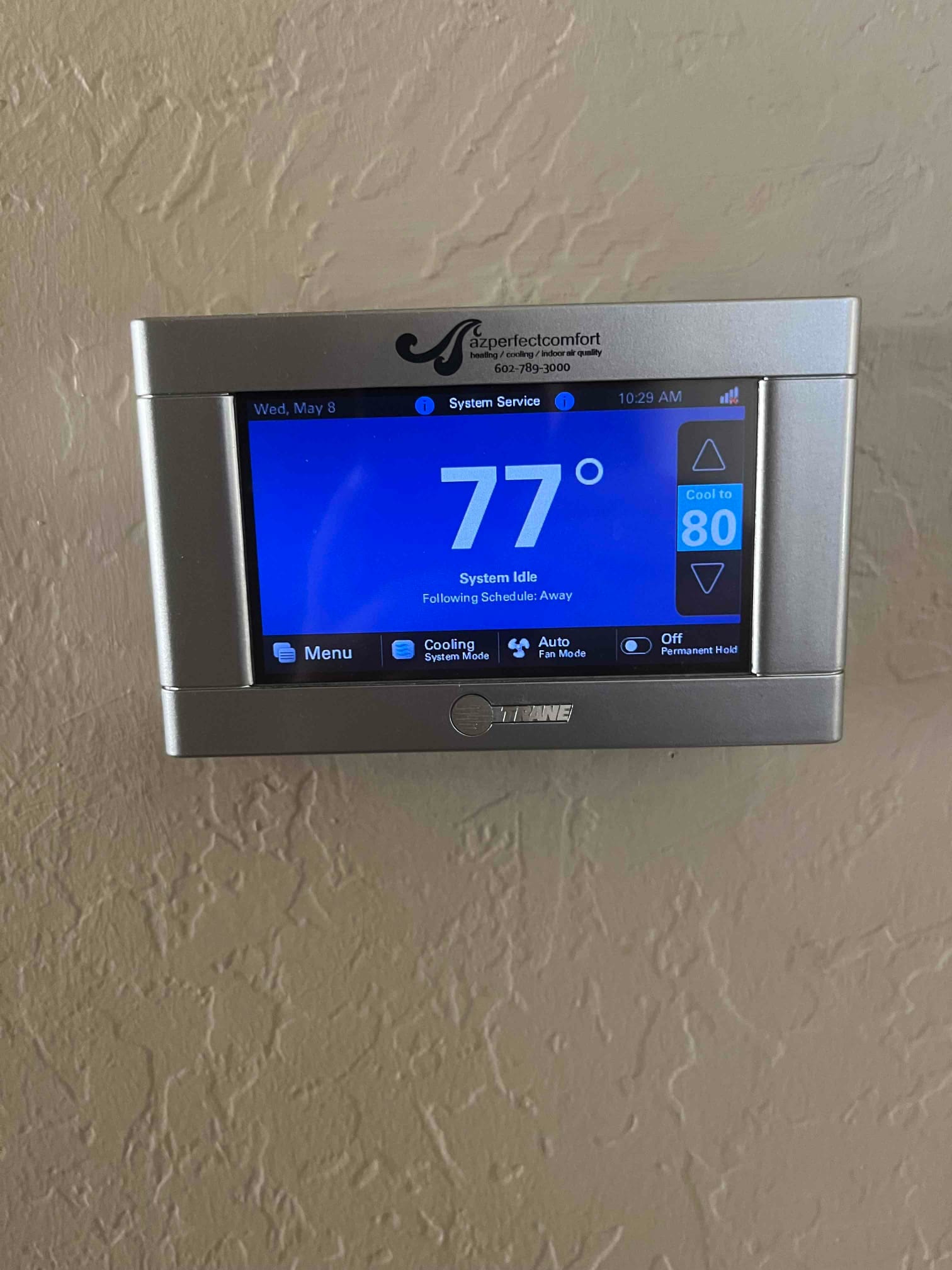 Wall-mounted touchscreen thermostat displays 77°F indoor temperature, cooling setpoint 80°F, system idle, and schedule set to Away.