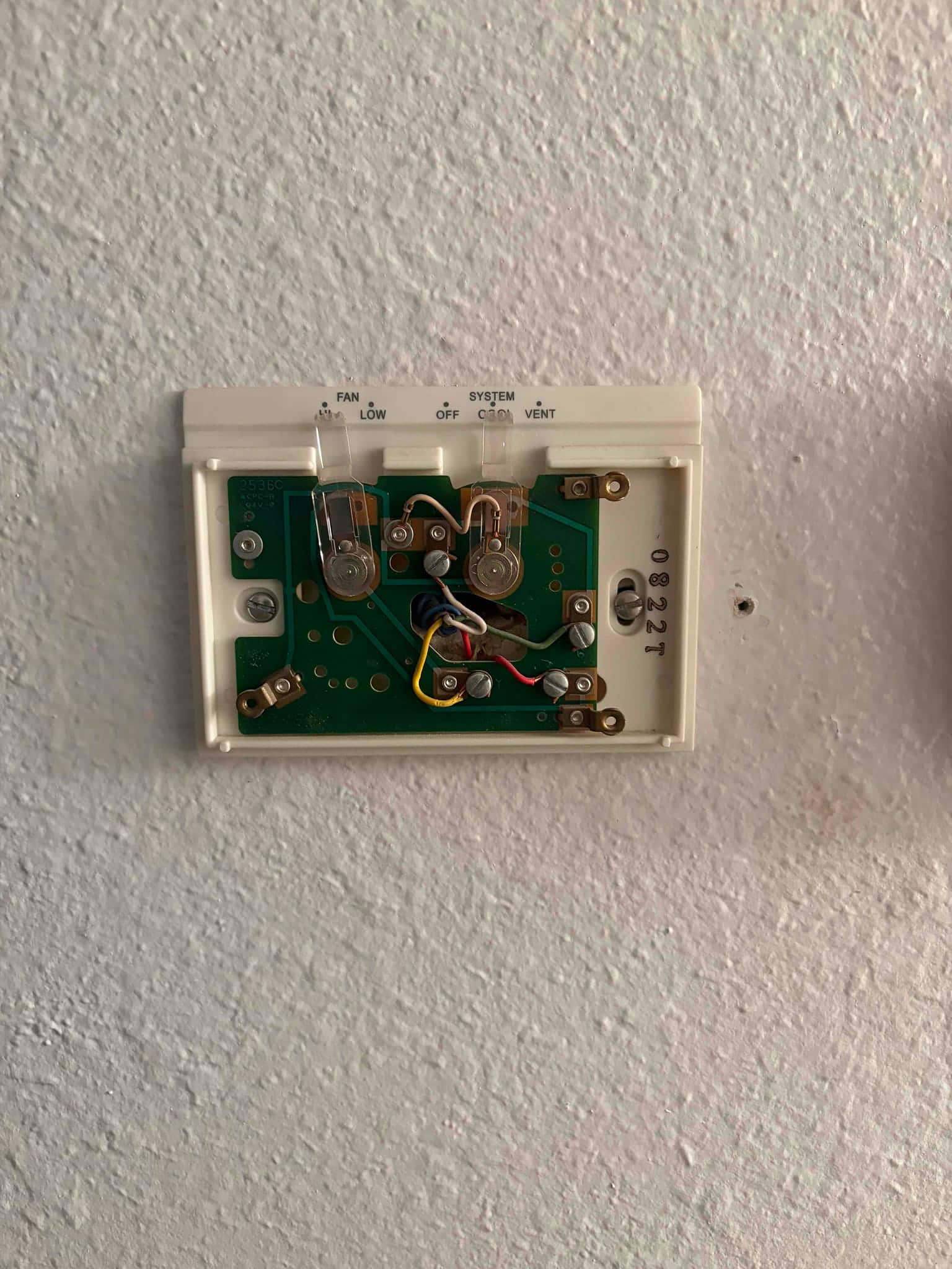 Wall thermostat with cover removed, showing wiring terminals, circuit board, and fan and system switch labels.