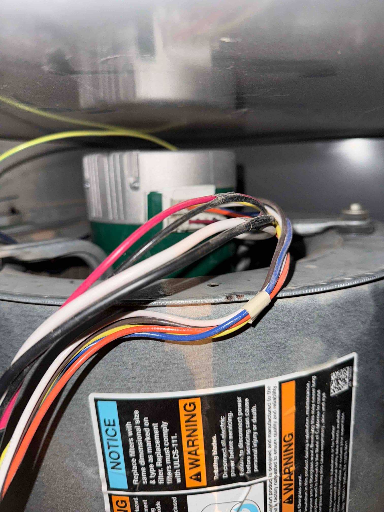 Blower motor assembly inside an air handler, showing multicolored wiring harness and safety warning labels.