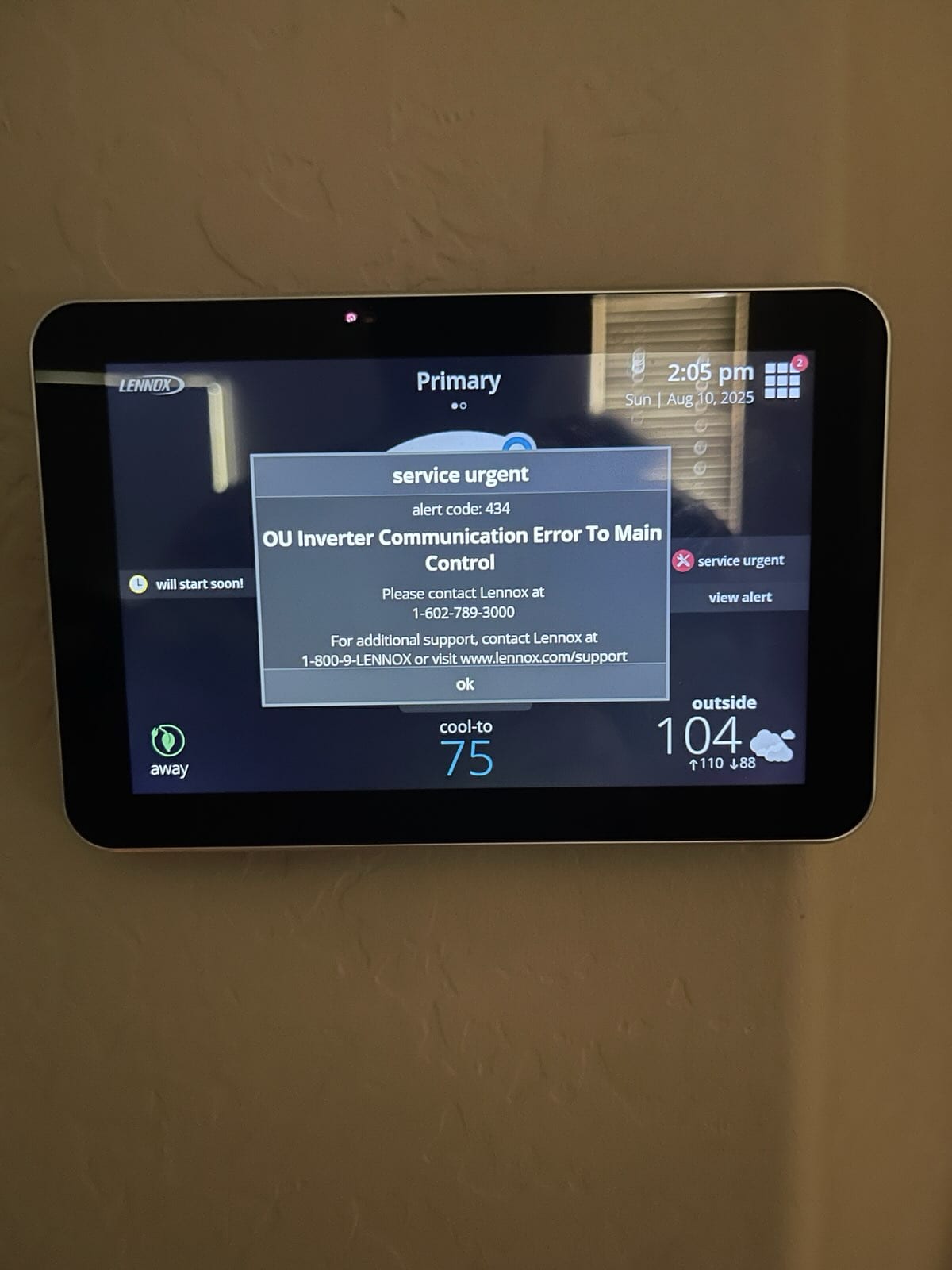 Wall-mounted touchscreen thermostat displays 'service urgent' alert code 434 and OU inverter communication error, set to cool-to 75, outside 104°F.