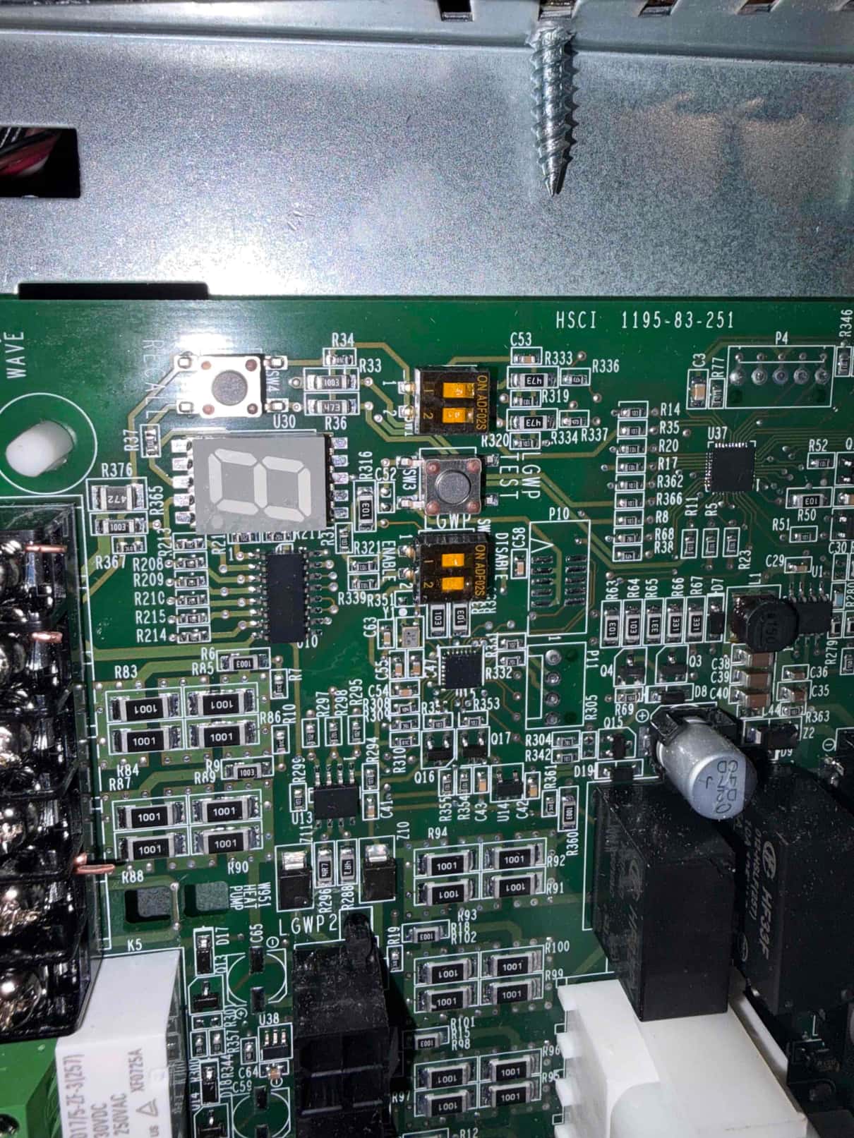 Furnace control board close-up showing seven-segment diagnostic display, push buttons, relays, and electrolytic capacitor.