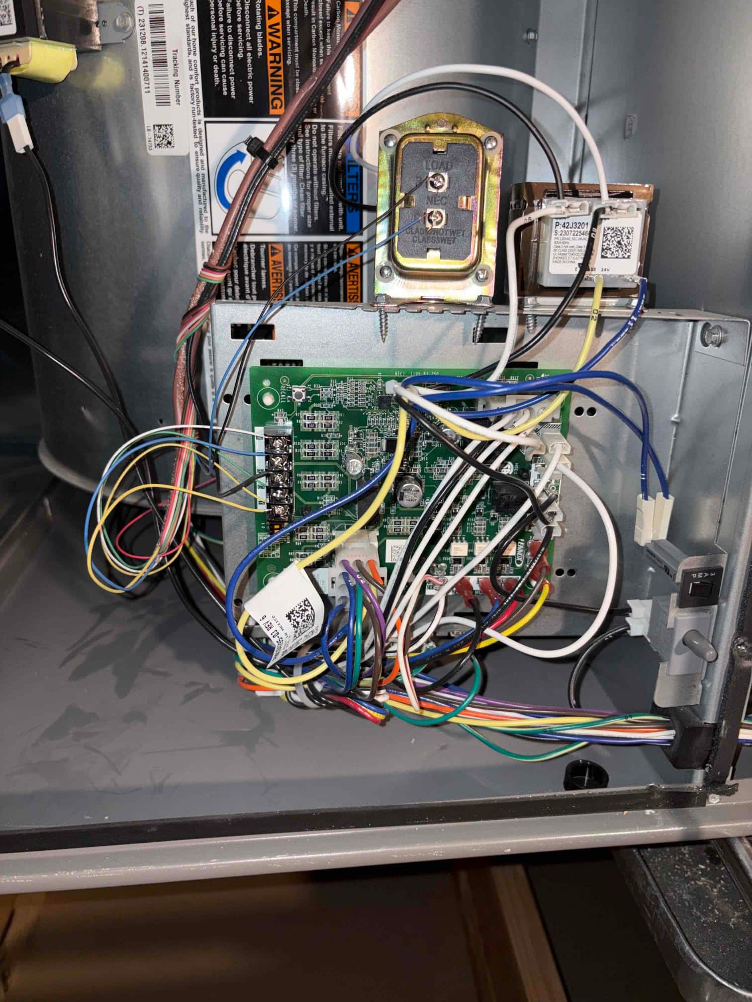 Furnace control compartment showing main circuit board, relays, and a 24V transformer with multiple connected low-voltage and high-voltage wires.