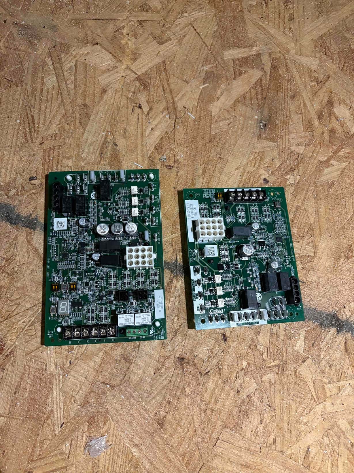 Two HVAC control boards with relays, capacitors, and labeled thermostat terminals W C R G Y O on plywood.