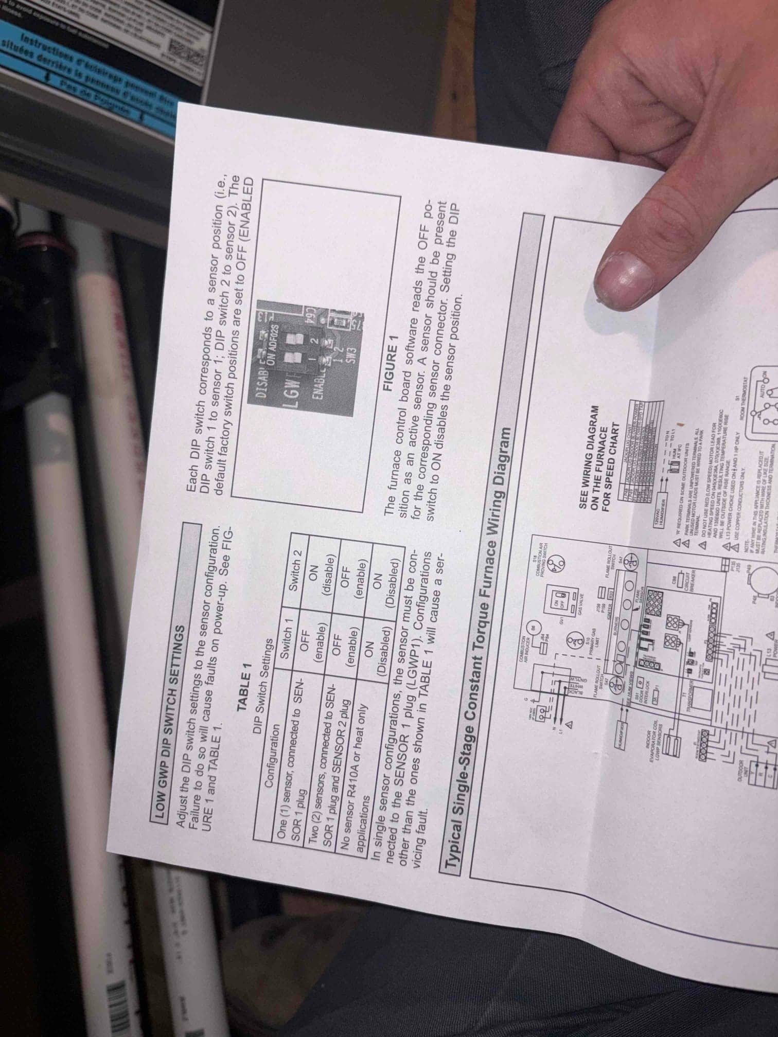 Technician holds furnace instruction sheet showing DIP switch settings and wiring diagram beside the open air handler cabinet.