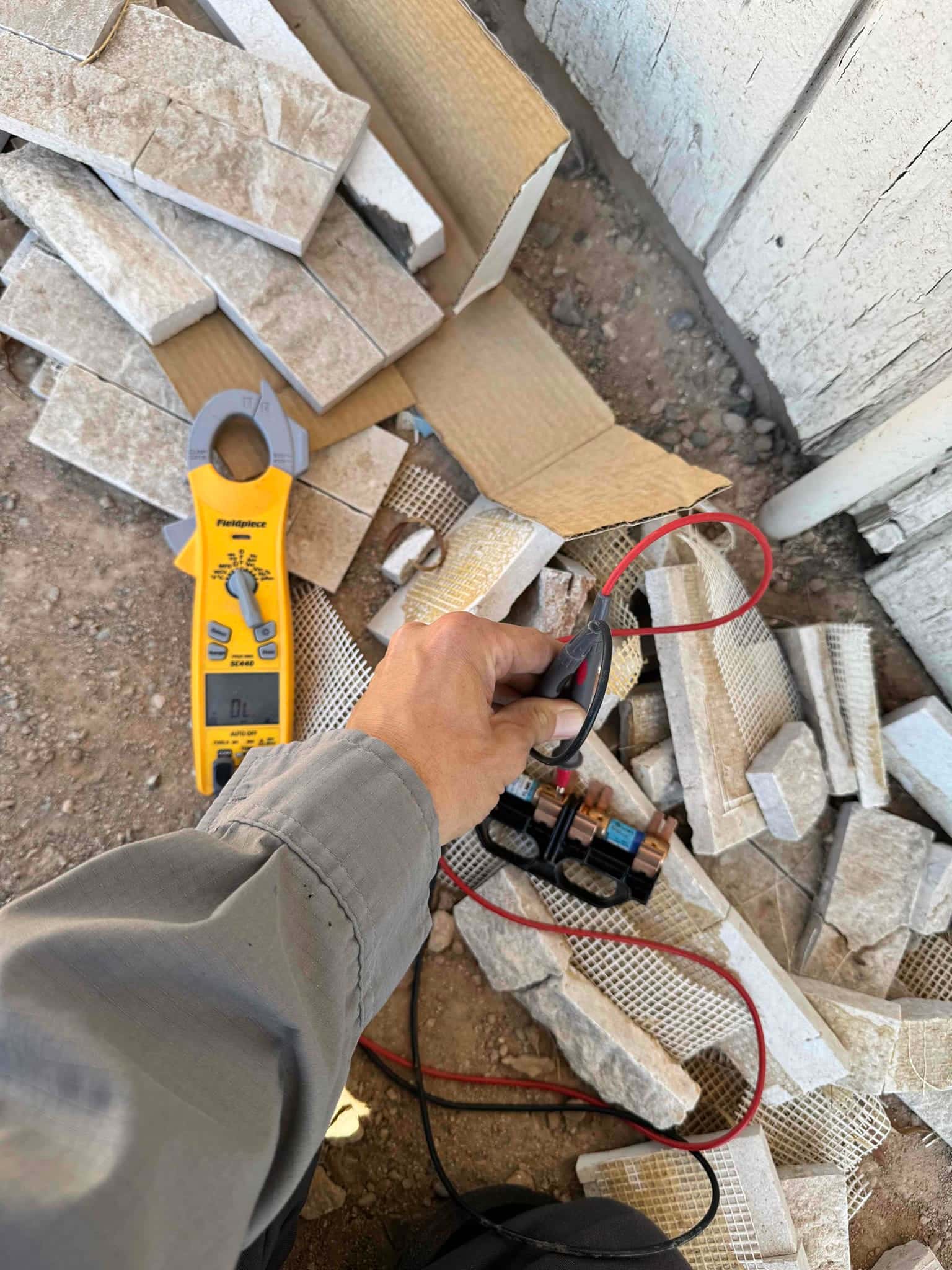 Clamp meter on the ground while test leads contact electrical terminals on a small component removed from equipment.