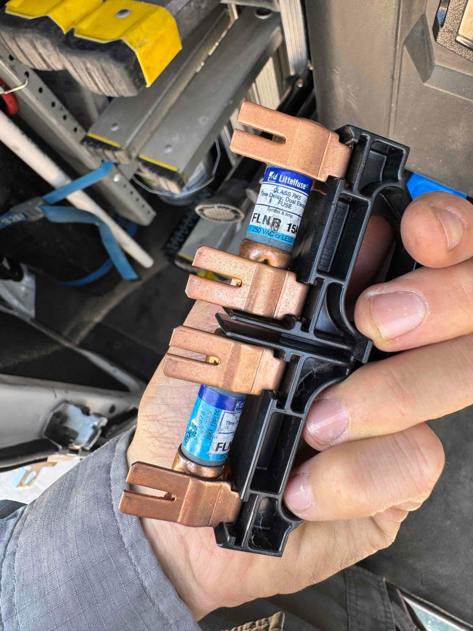 Hand holding a fuse holder with two fuses labeled FLNR 15 and 250 VAC OR LESS.
