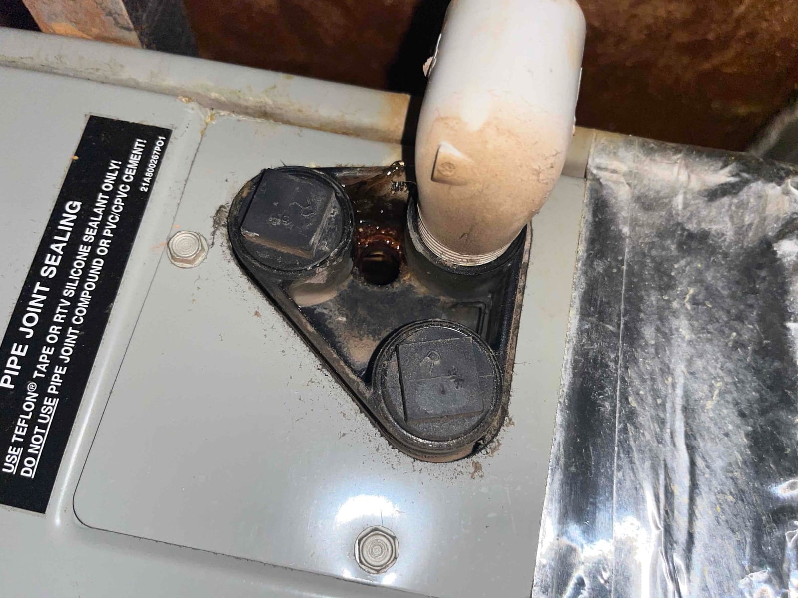 Air handler condensate drain elbow with two capped cleanouts on top of cabinet, with rust and dust visible.