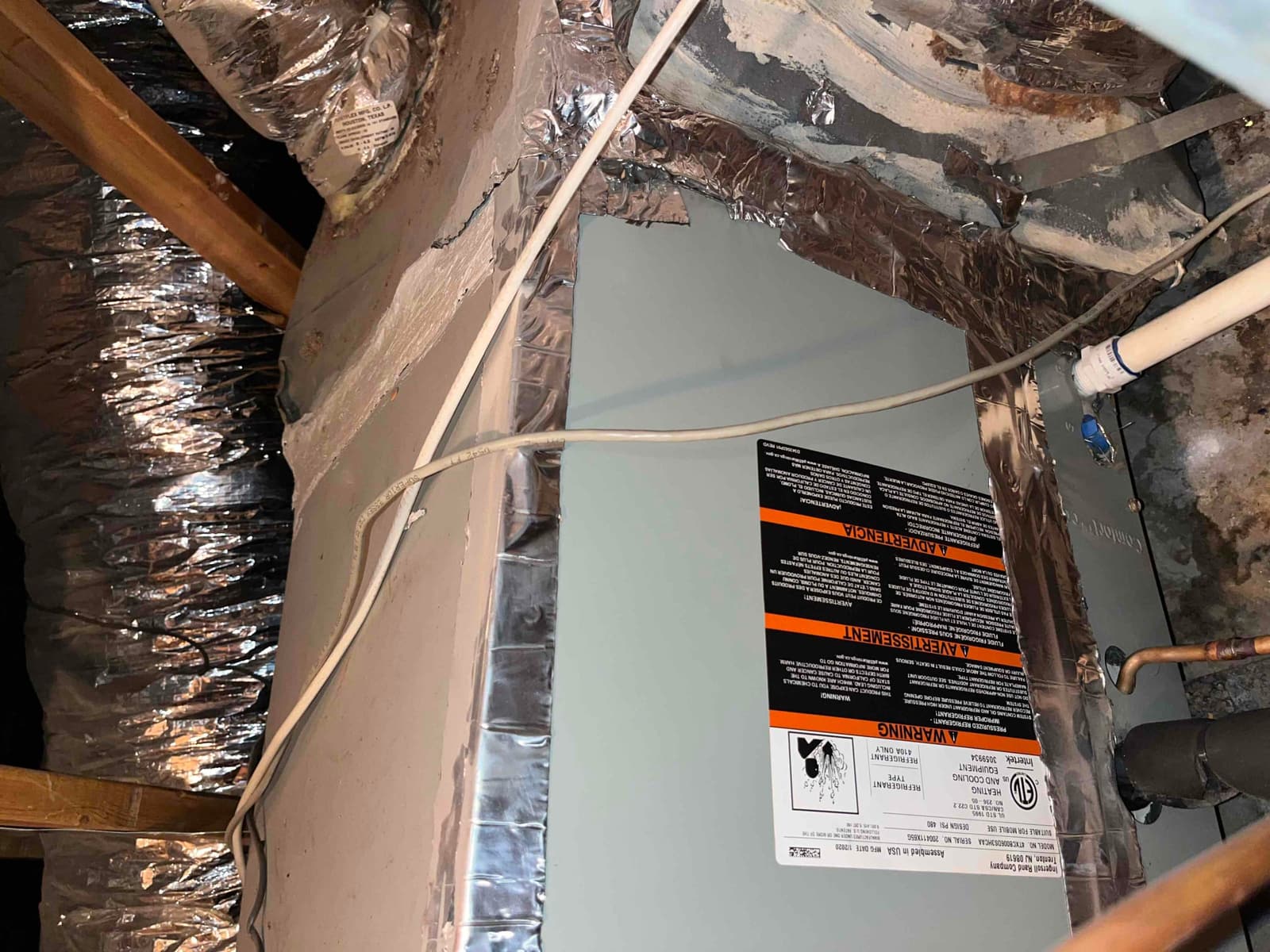 Attic air handler cabinet with foil-taped connections, flexible ductwork, PVC condensate drain, and insulated refrigerant lines visible.