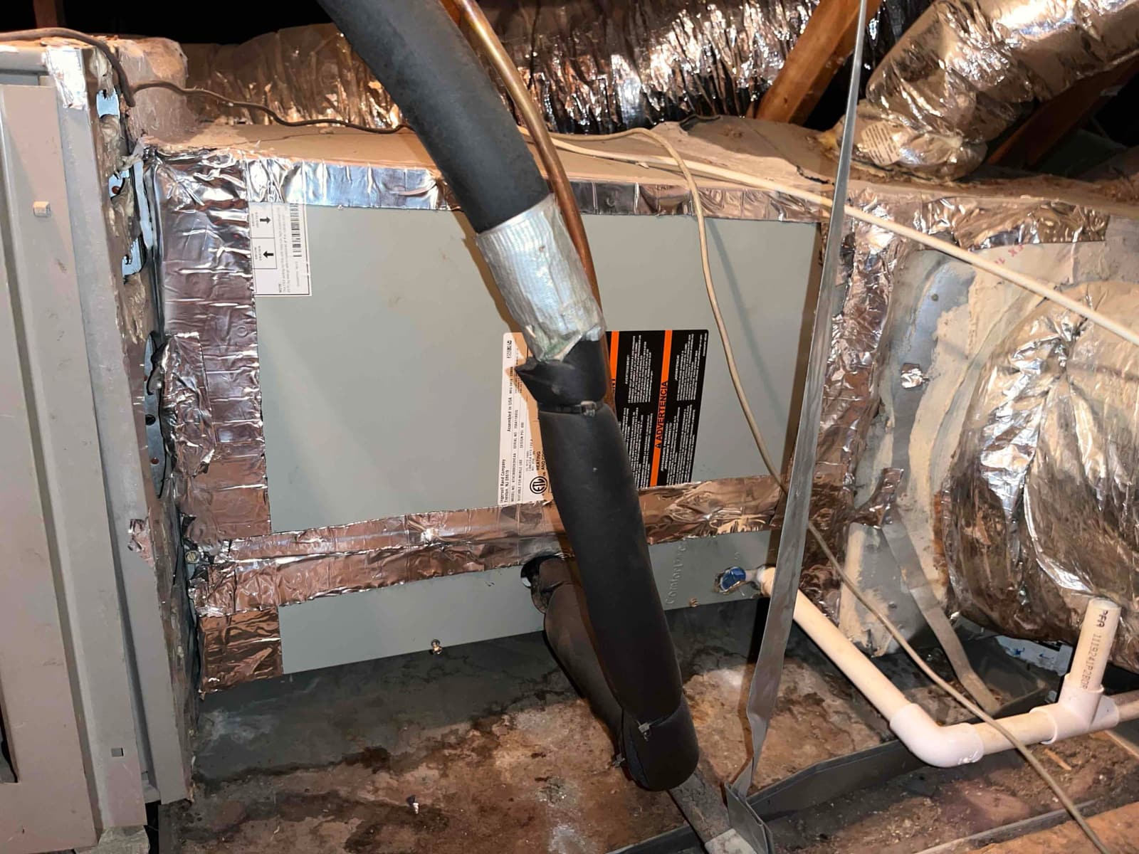 Attic air handler with foil-taped panels, insulated refrigerant line, and PVC condensate drain connected to ductwork and plenum.