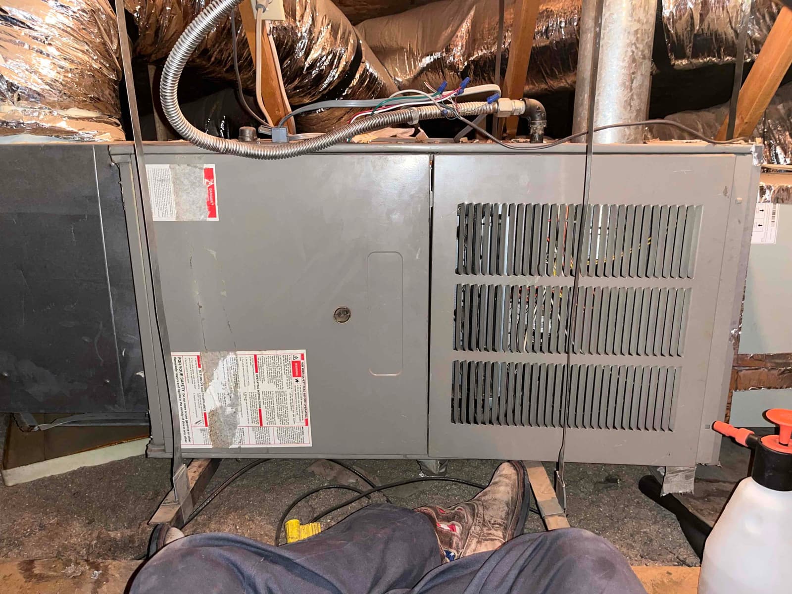Attic-mounted furnace cabinet with louvered access panel, flex duct connections, metal flue, and control wiring visible across the top.