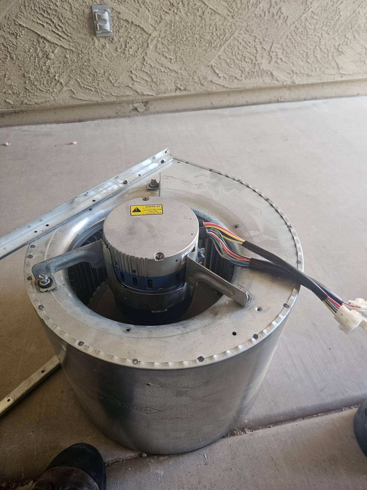 Blower motor and wheel assembly on the ground, showing metal housing with rotation arrow, wiring harness, and mounting bracket.