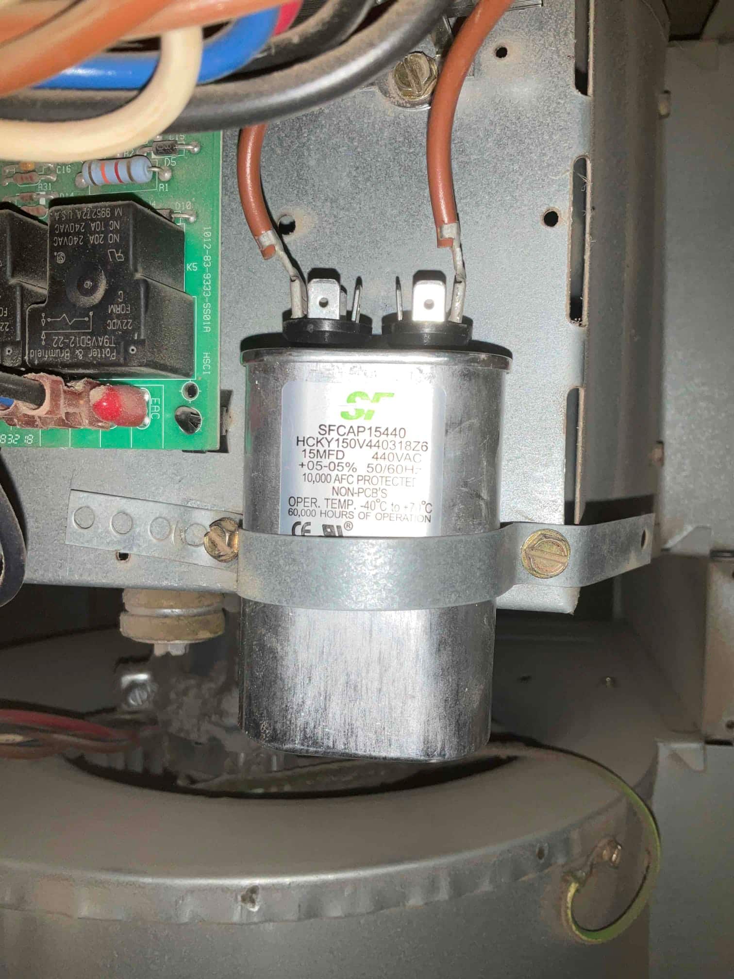 Capacitor labeled 15 MFD 440VAC mounted inside the furnace assembly, with two brown wires connected to its terminals and retaining strap.