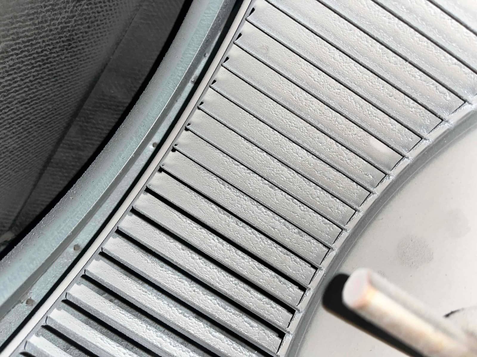 Close-up of an HVAC blower wheel, showing dust buildup on the metal fins inside the air handler housing.