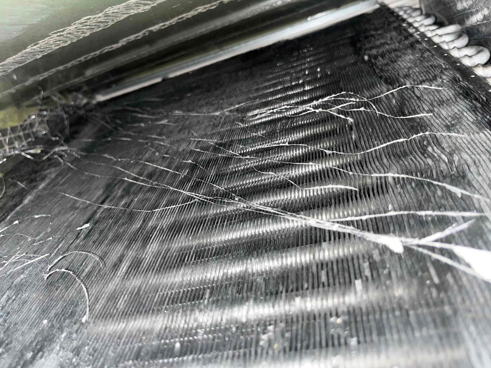 Close-up of HVAC coil fins with strands of debris and dust across the surface.