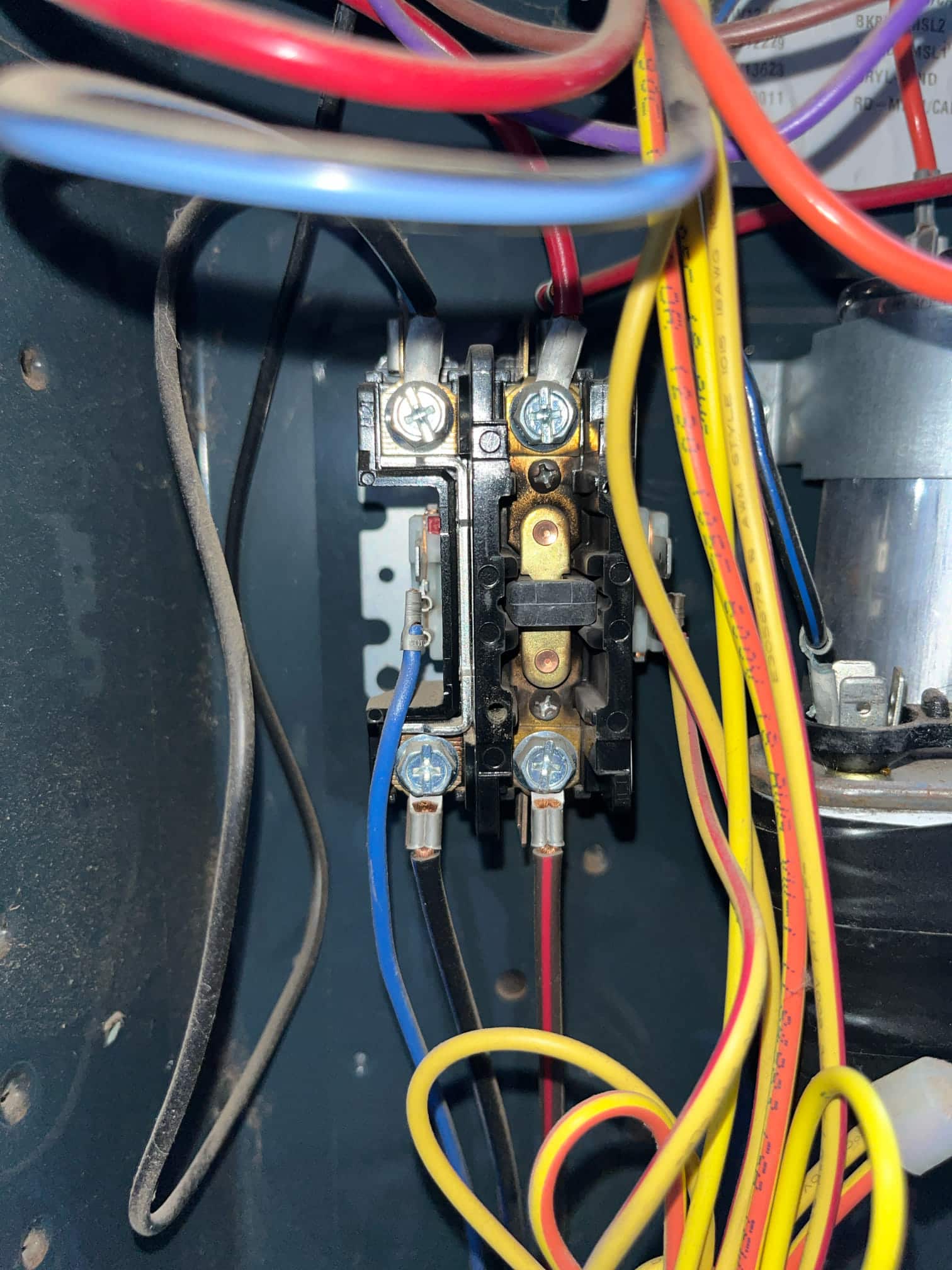 Close-up of an HVAC contactor with red, blue, black, and yellow wiring connected inside the condenser cabinet.