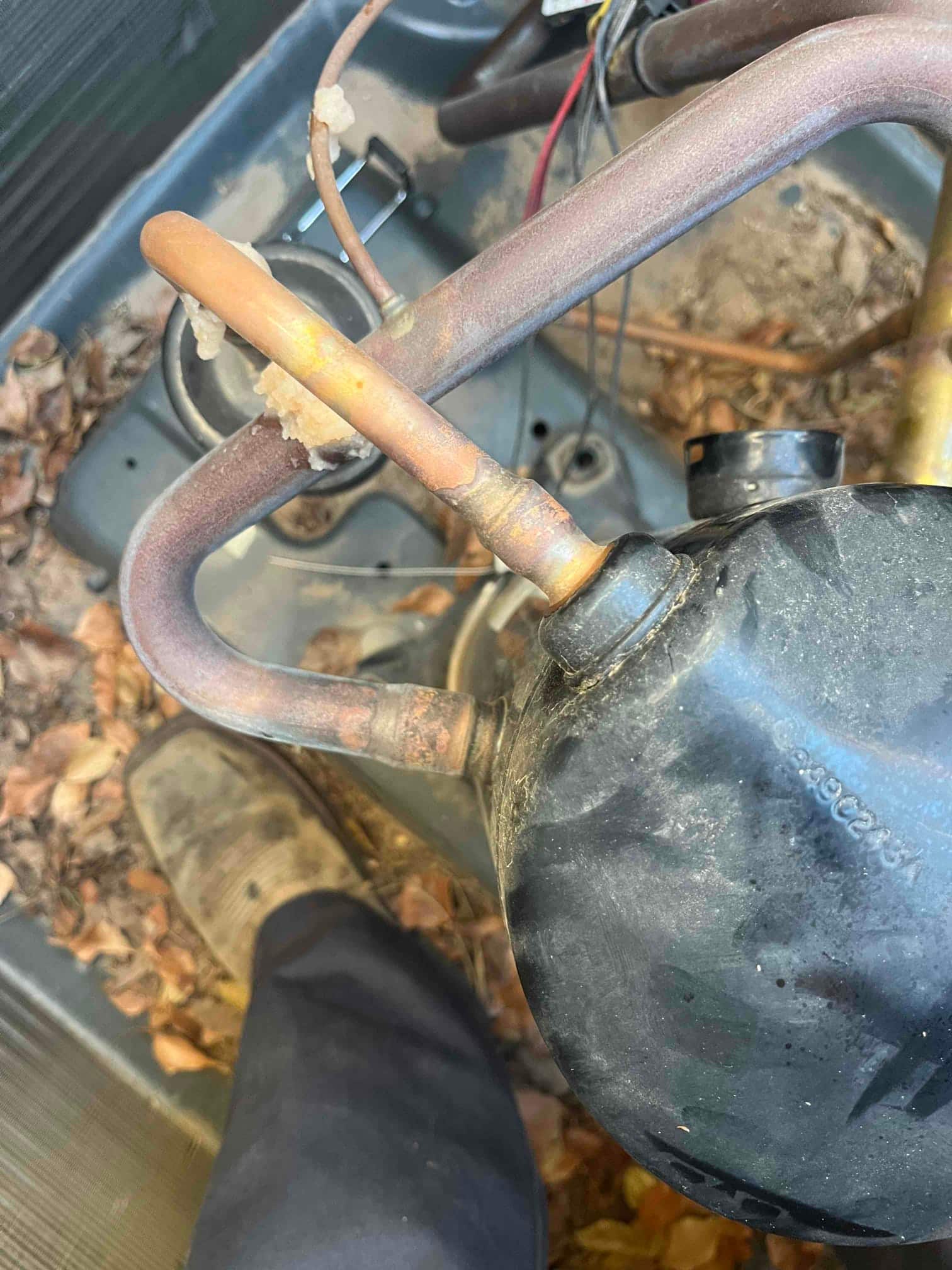 Compressor and copper refrigerant lines inside outdoor unit, showing brazed joints and insulation residue, with leaves in base pan.