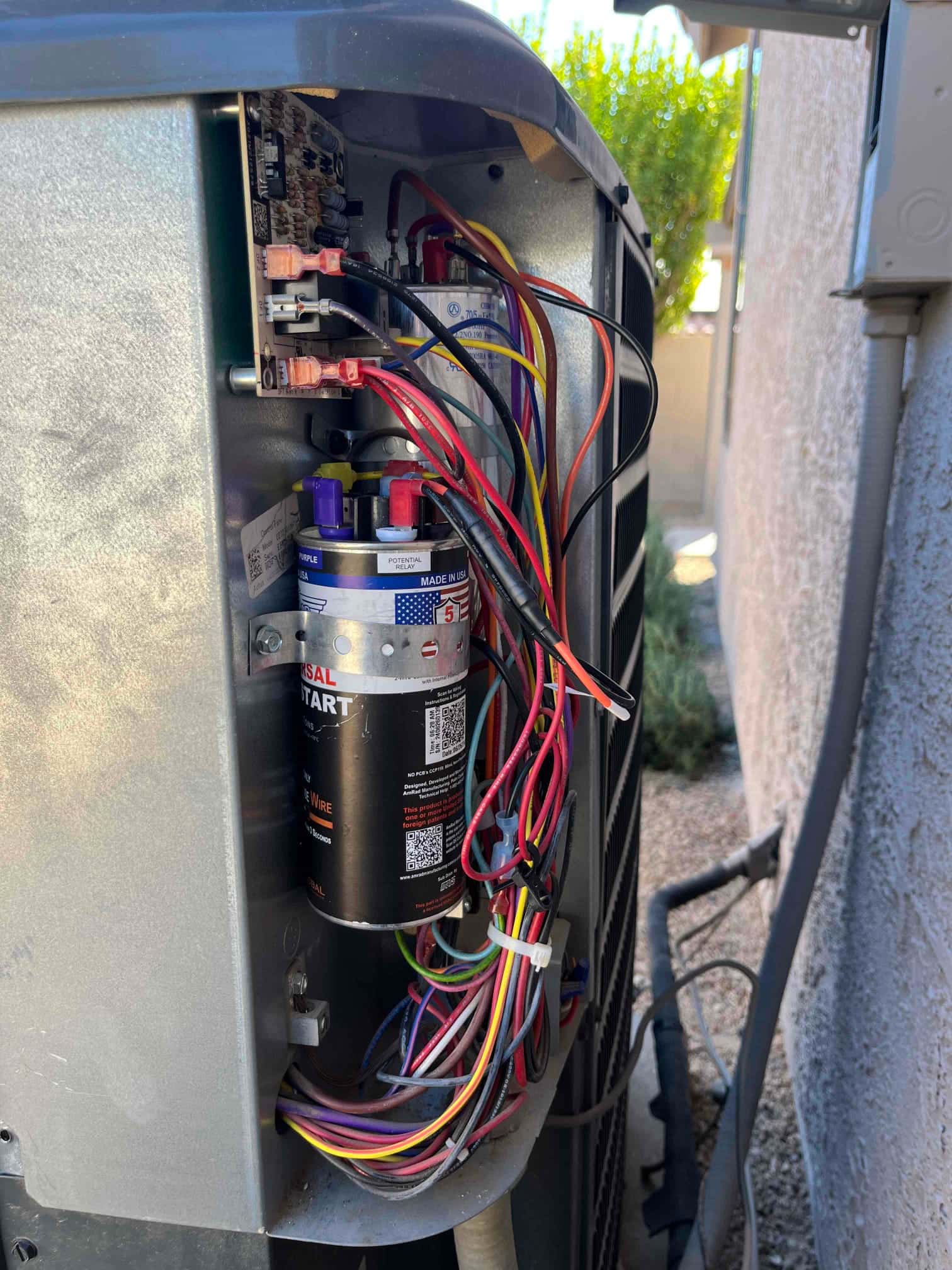 Condenser electrical compartment open, showing dual-run capacitor, hard-start kit, control board, and connected wiring.
