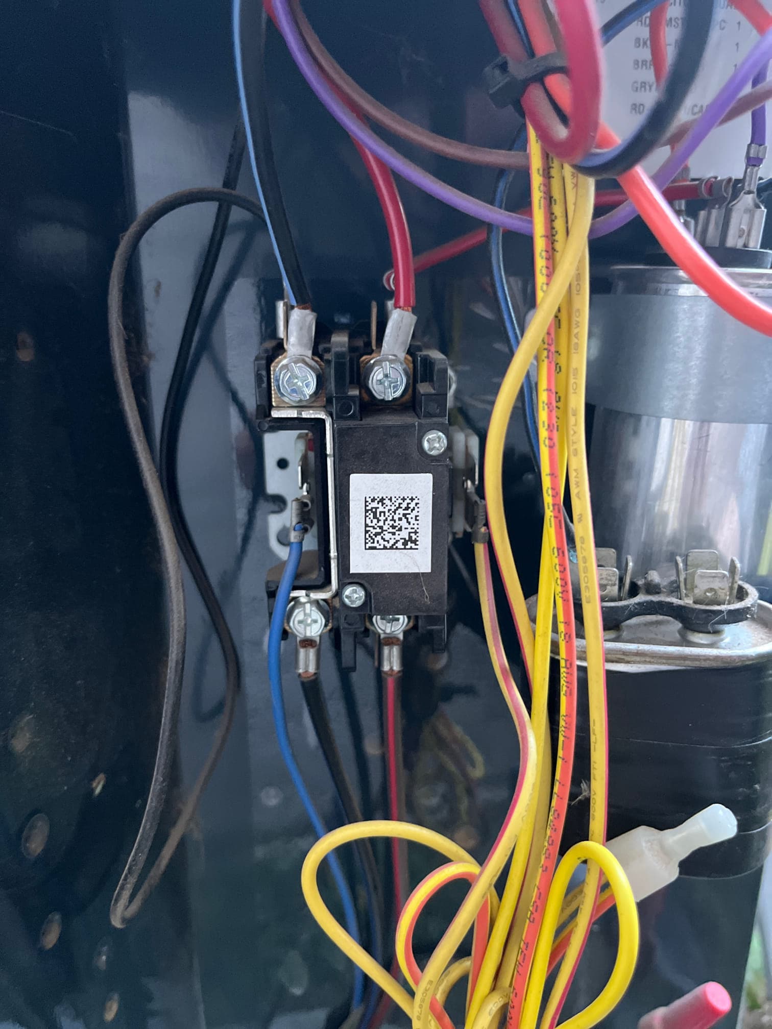 Contactor with multiple wires connected inside the outdoor condenser cabinet, with a round capacitor and wiring harness visible to the right.