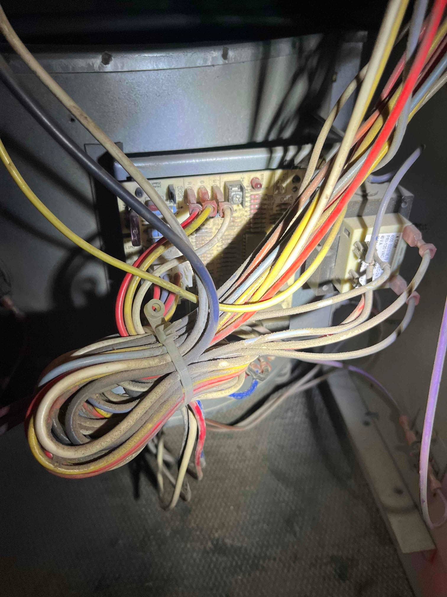 Control board inside air handler showing multiple colored wires connected and bundled, with dust on wiring and components.