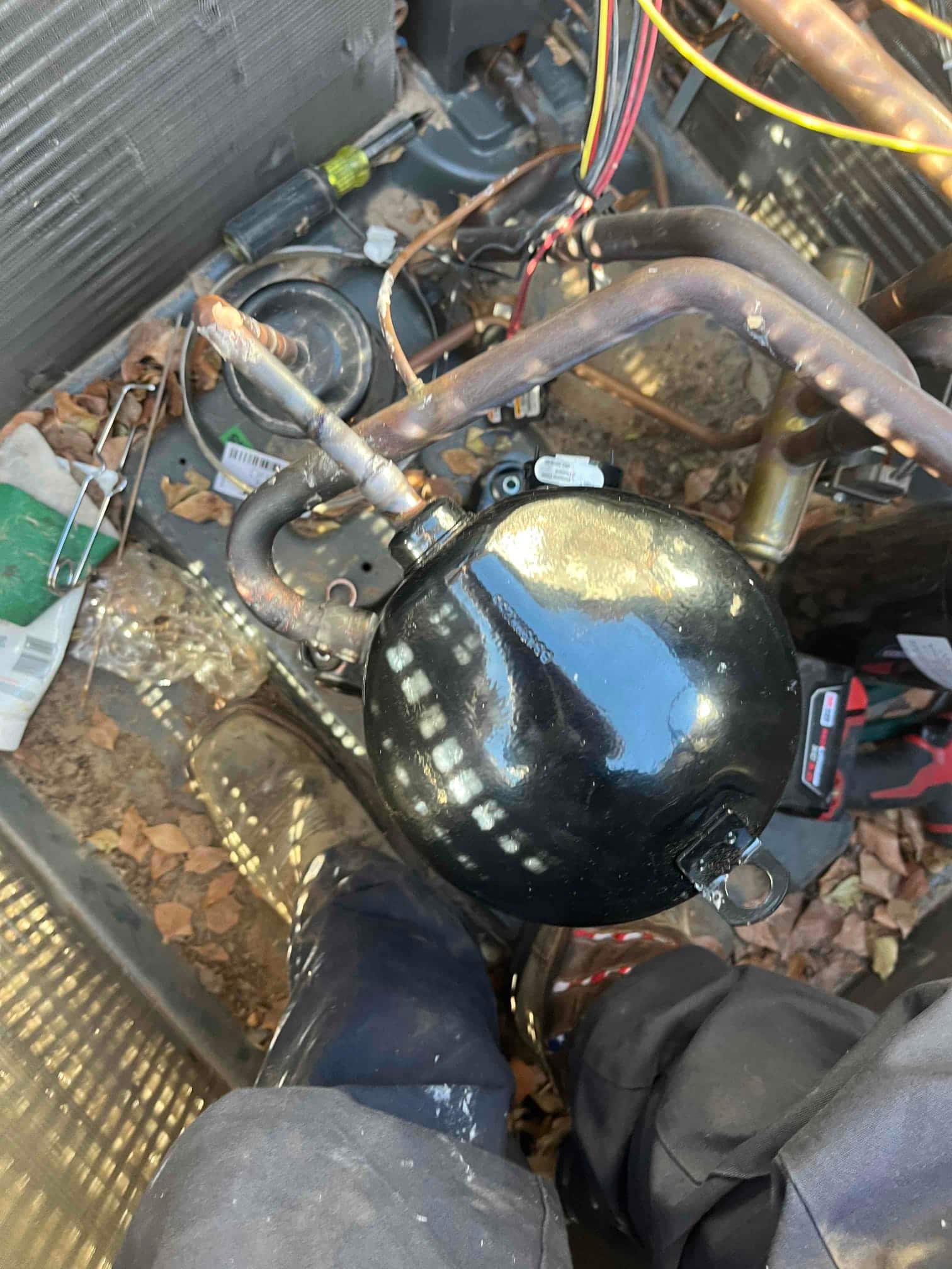 Copper refrigerant lines with a black spherical component inside the outdoor condenser cabinet, with tools and wiring visible during service.