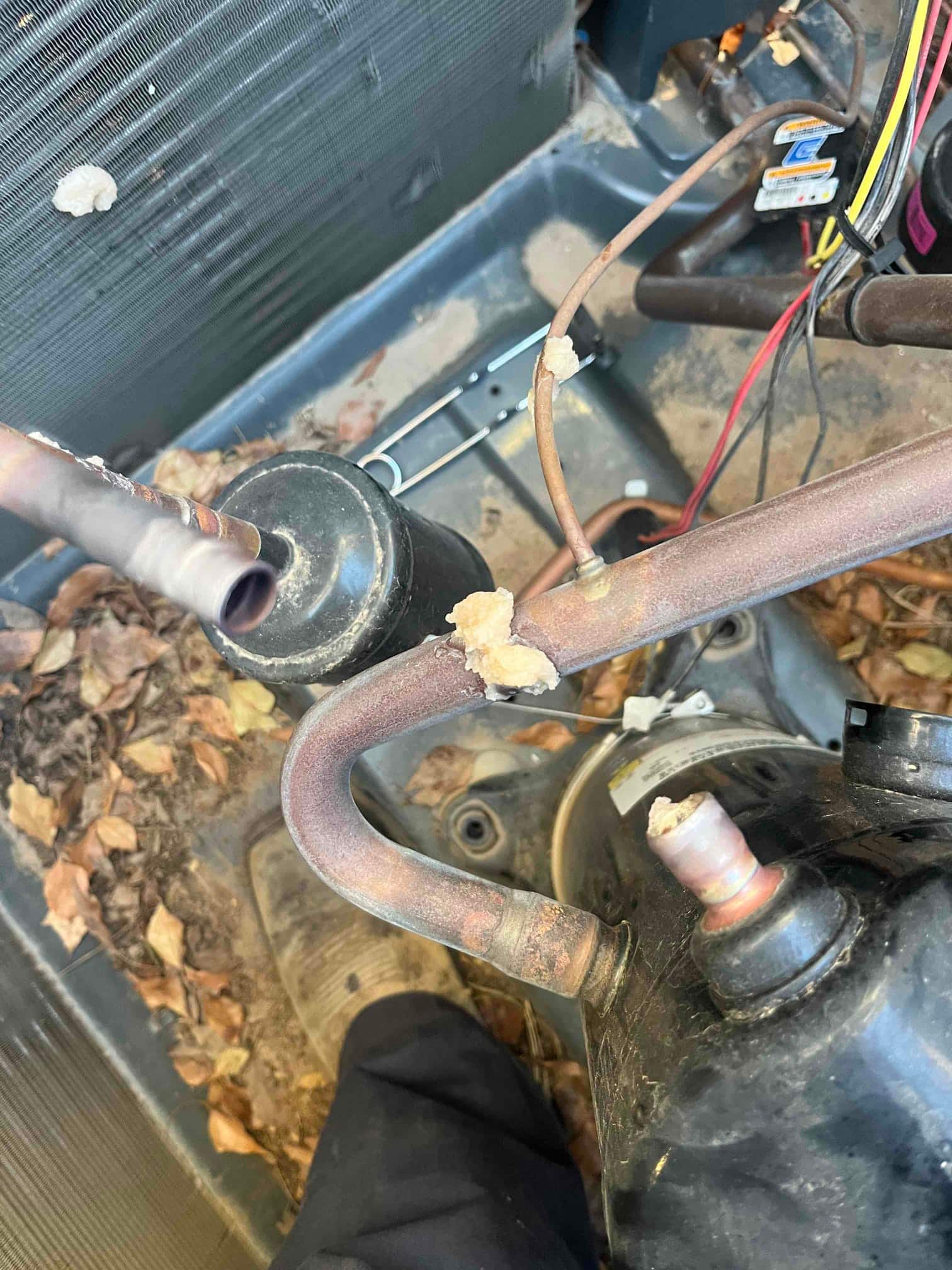 Copper refrigerant lines and compressor inside outdoor condenser, with brazed joints and sealant residue visible.