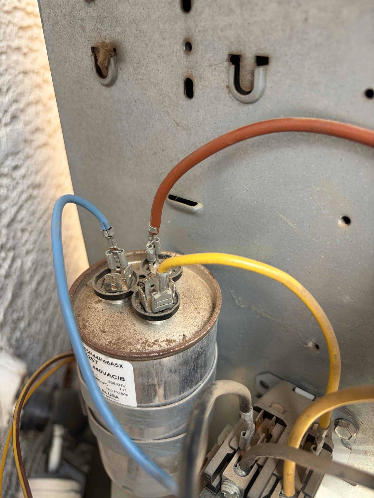 Dual-run capacitor with connected blue, brown, and yellow wires; label shows 440 VAC rating; dust present on top.